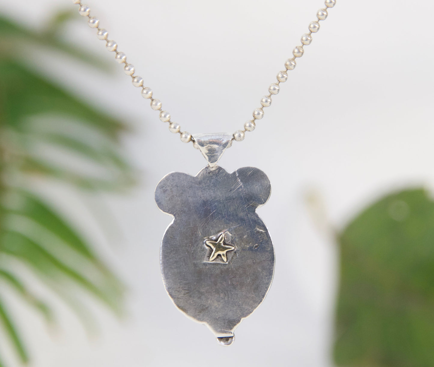 Necklace with a pendant featuring a star design, against a blurred green leafy background.
