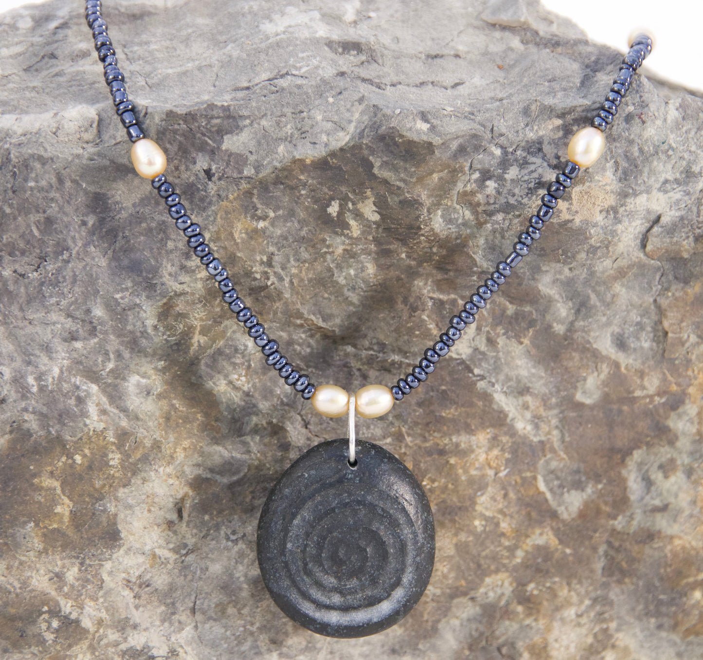 Necklace with a black spiral pendant on a rock background