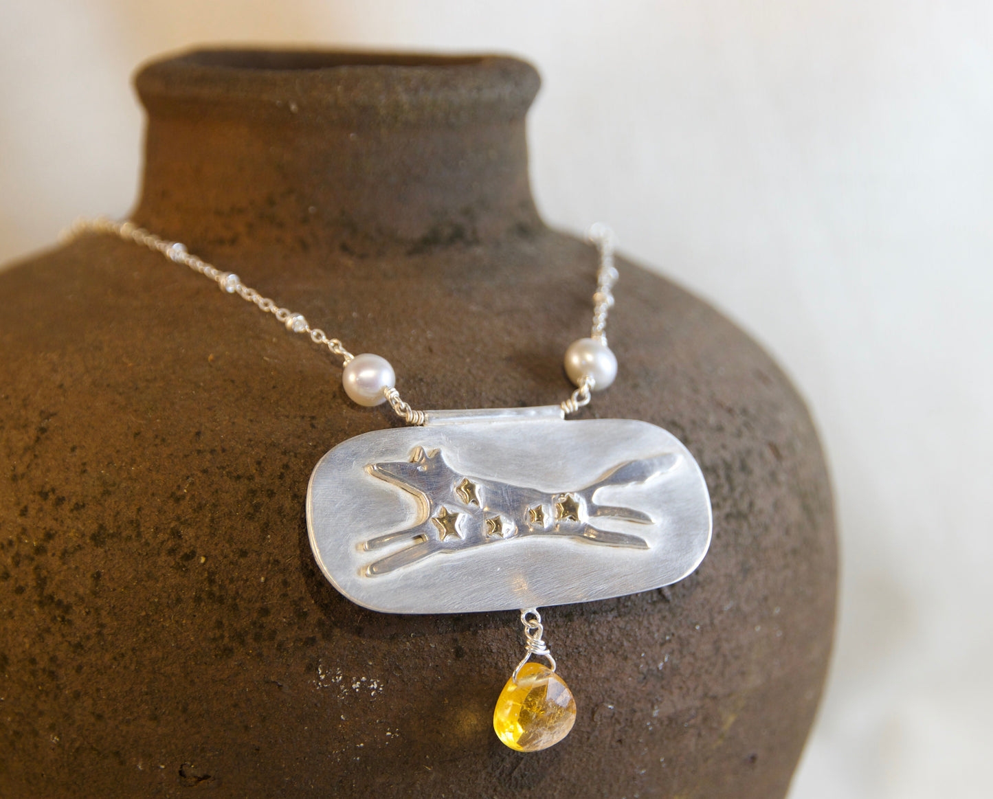Necklace with a pendant on a textured brown vase against a white background