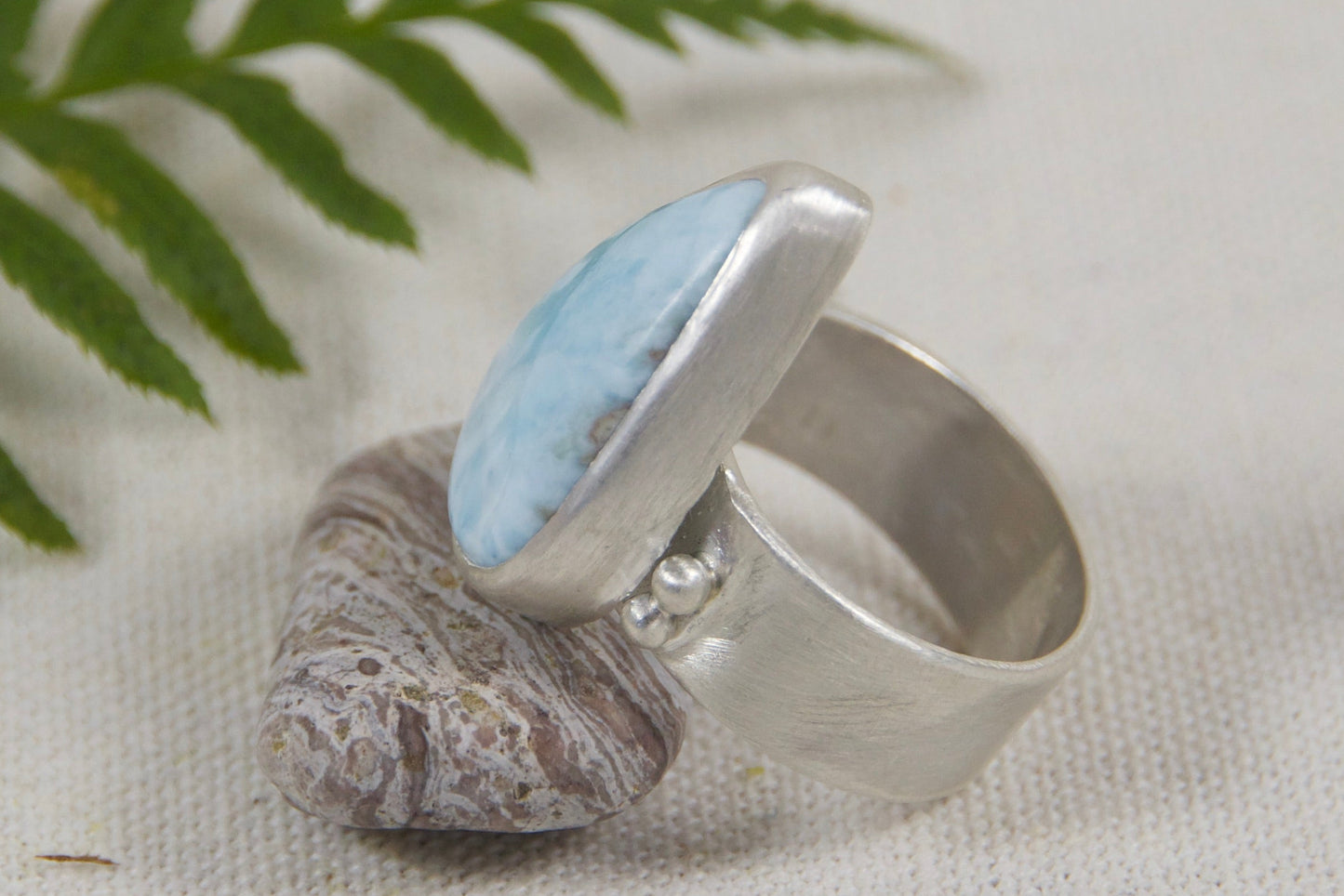 Silver ring with textured design on a light background with a fern leaf