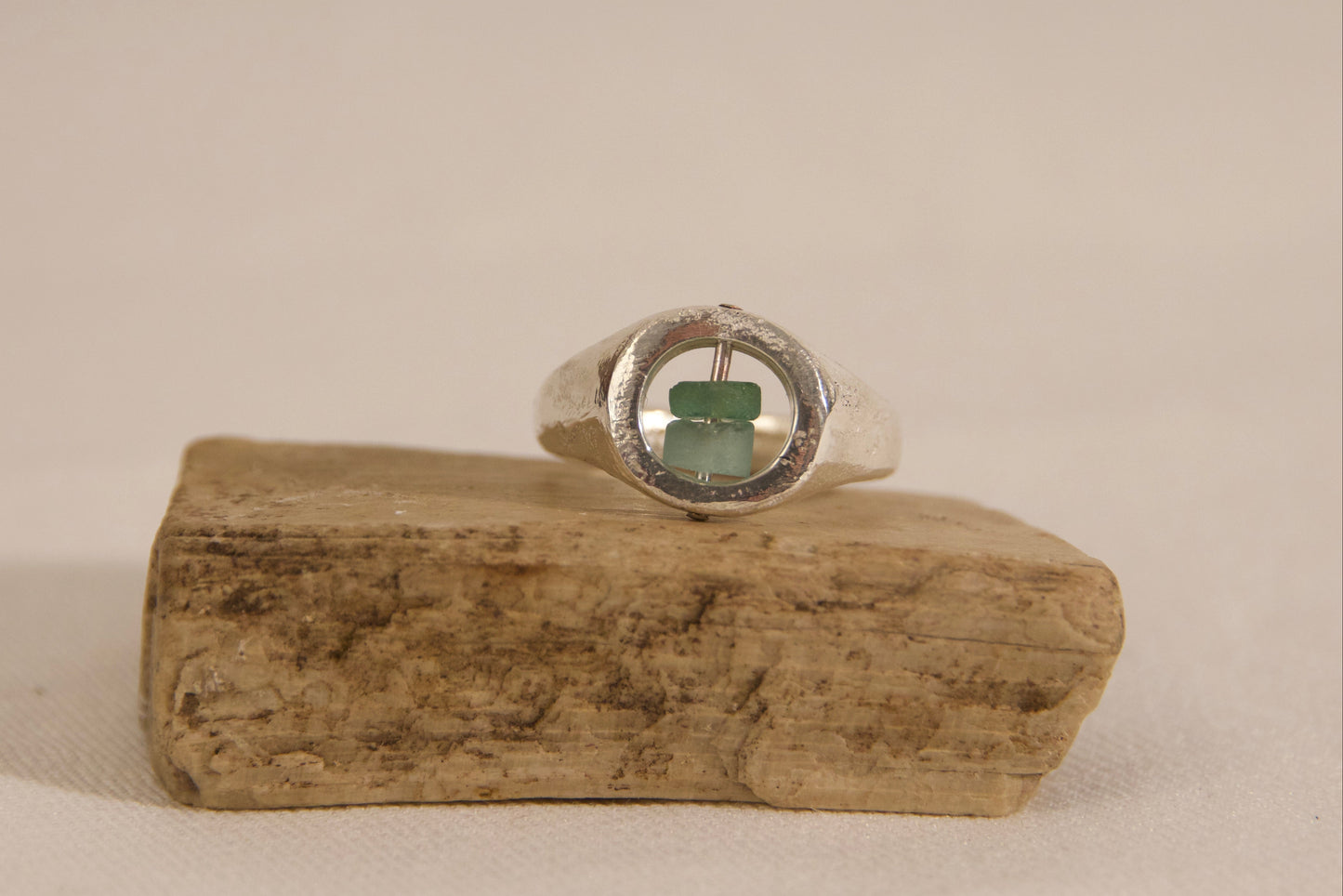 Silver ring with a green stone on a wooden block against a beige background