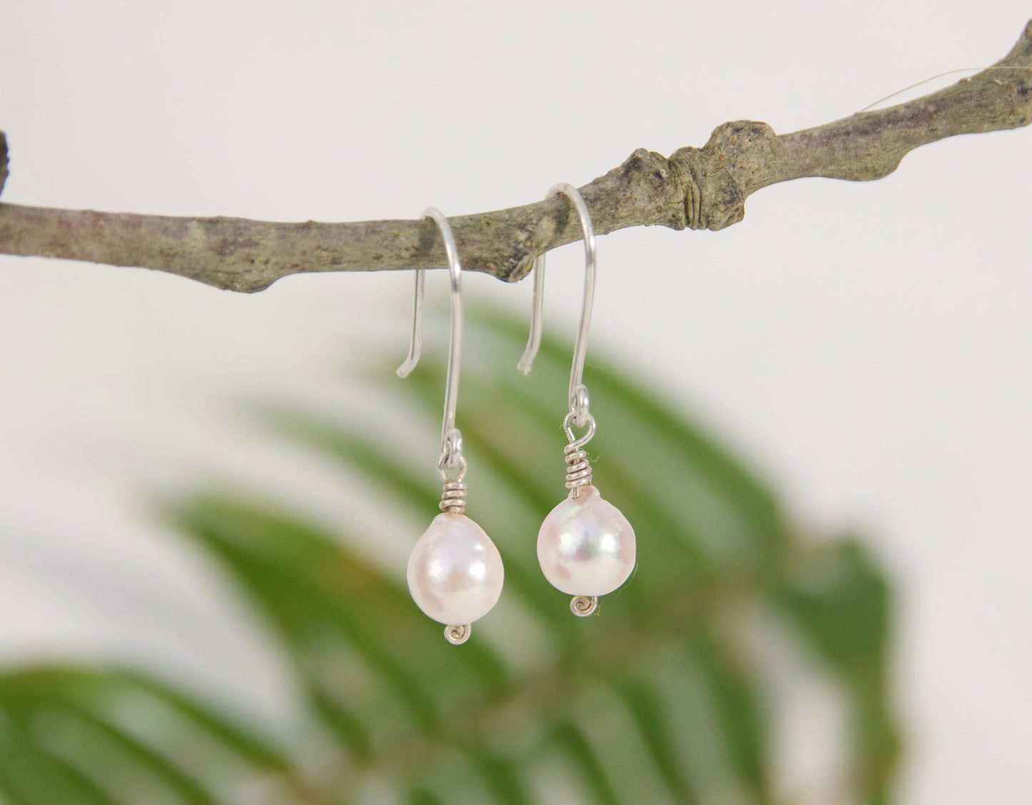 Pearl earrings hanging from a branch with a blurred natural background