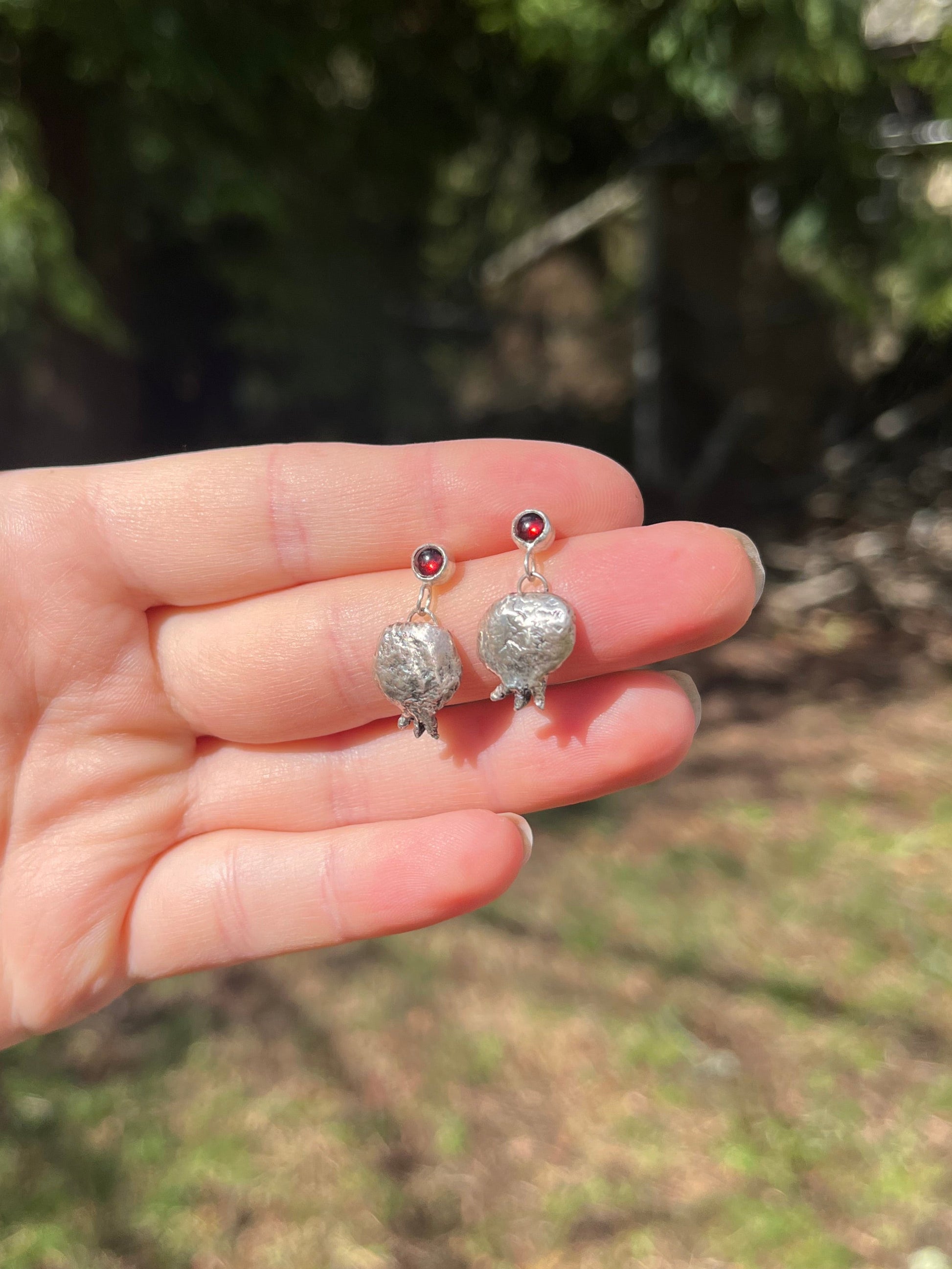 Handcrafted sterling silver pomegranates handing from richly red garnets in the sunlight 
