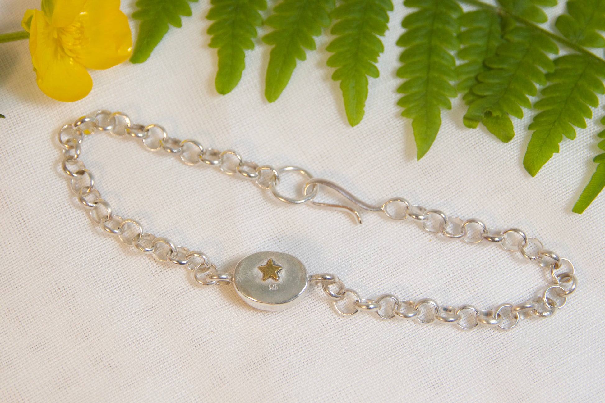 Silver bracelet with a star charm on a white fabric background with green leaves and a yellow flower.