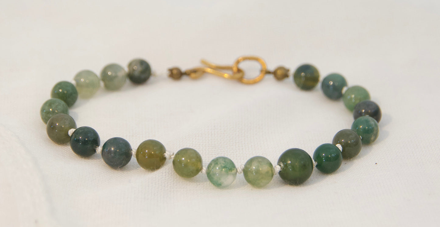 A beaded bracelet made of round green and gray stone beads with a gold-tone clasp, displayed on a plain white background.