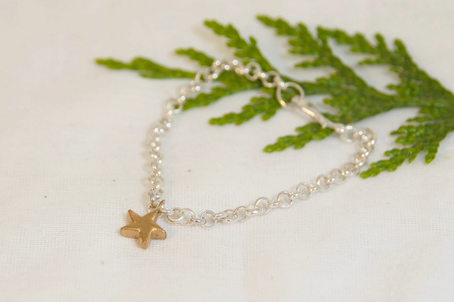 Silver bracelet with a gold star charm on a white surface with green leaves.