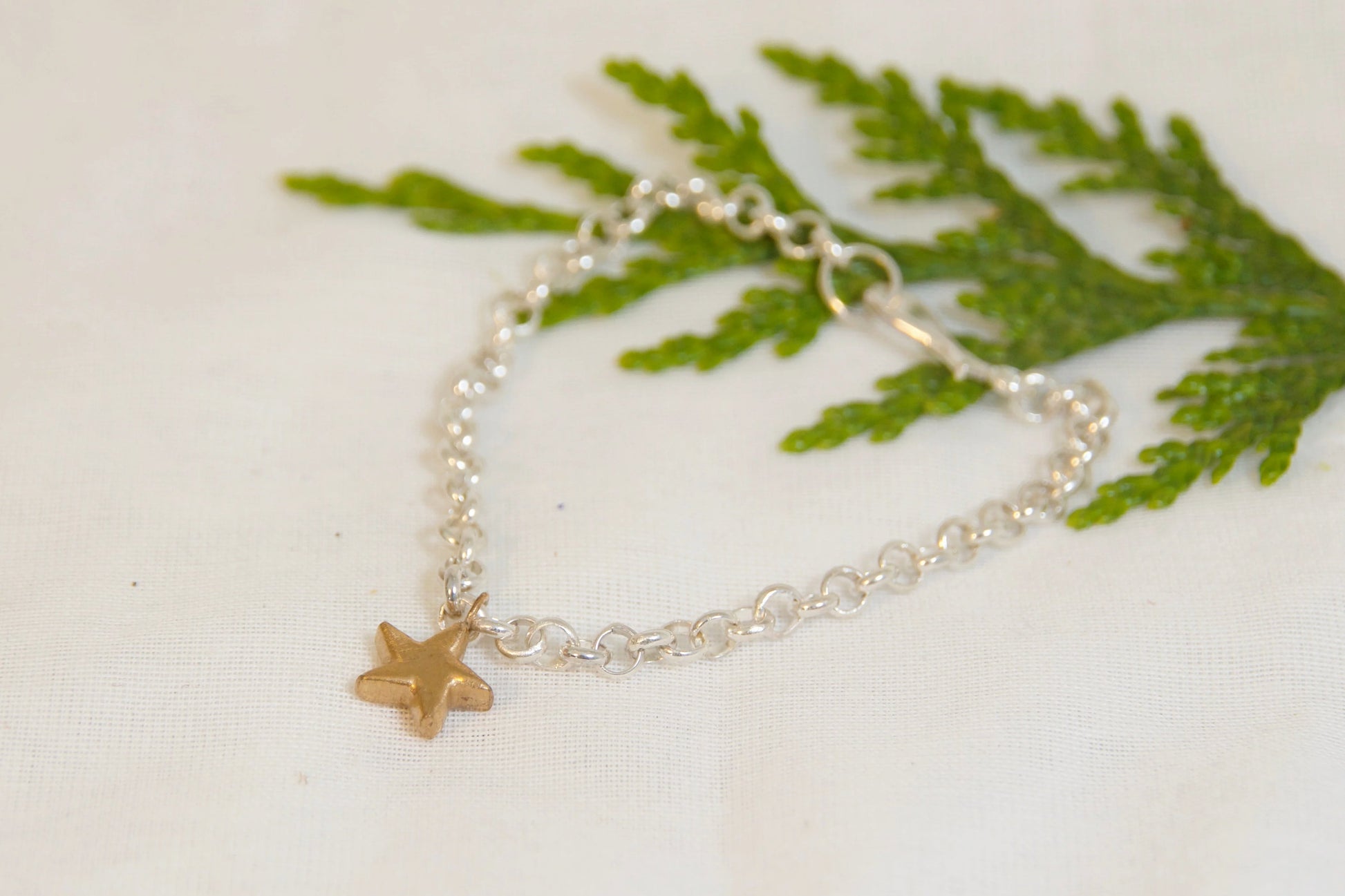 Silver bracelet with a gold star charm on a white surface with green leaves.