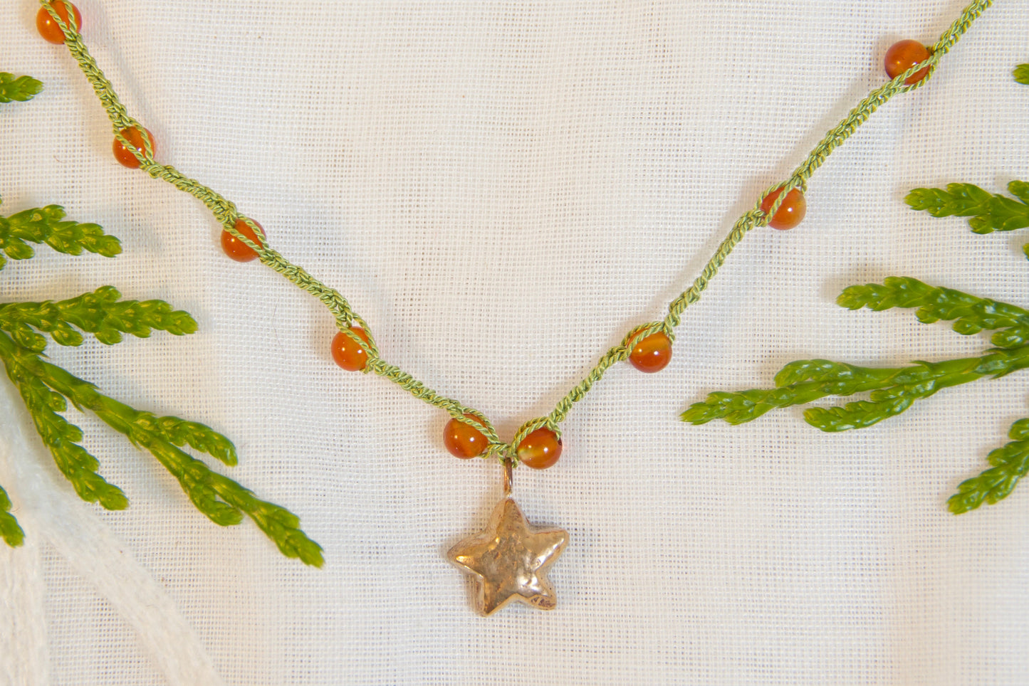 Necklace with green beads and a star pendant on a white fabric background