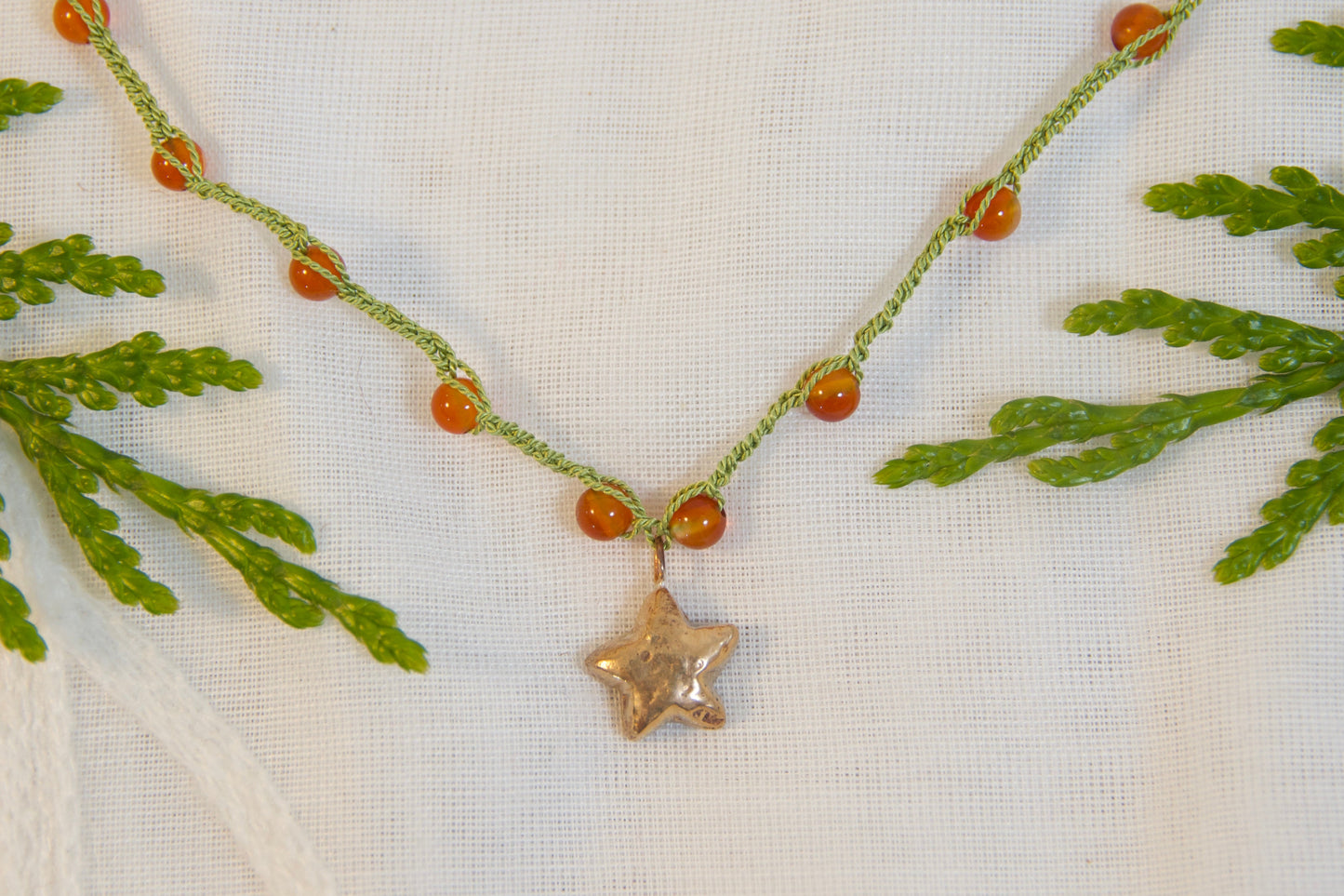 Necklace with a star pendant on a white fabric background with green leaves.