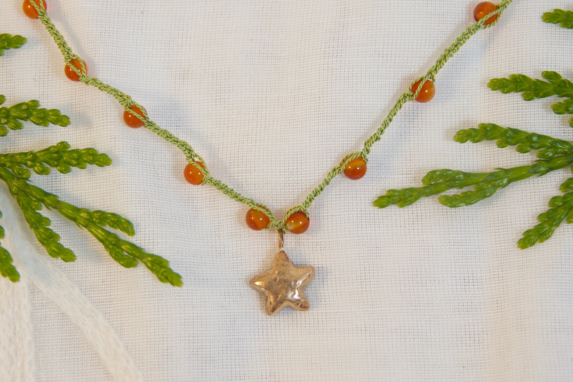 Necklace with a star pendant on a white fabric background with green leaves.