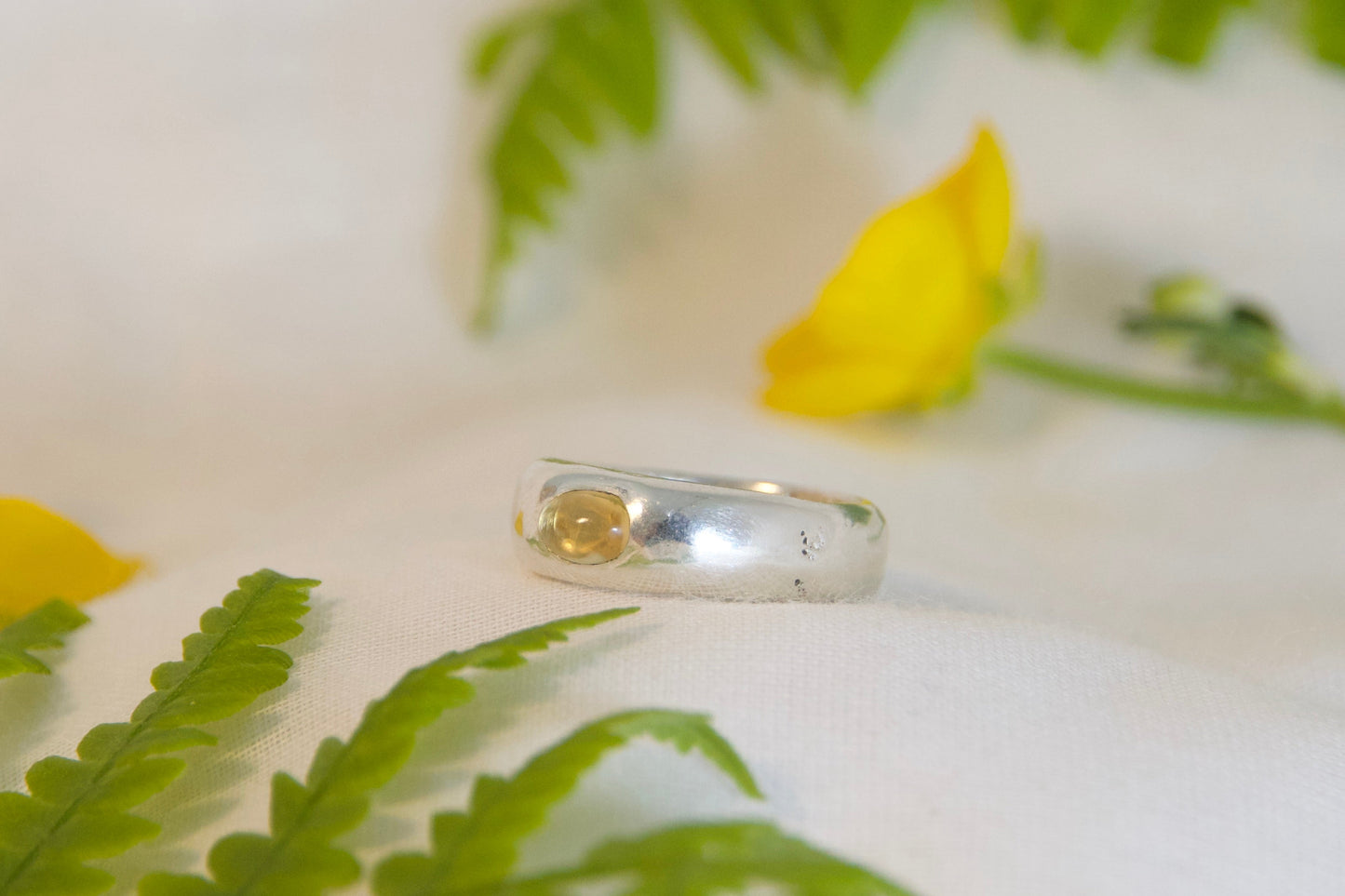 Silver ring with green fern leaves and yellow flowers on a white background