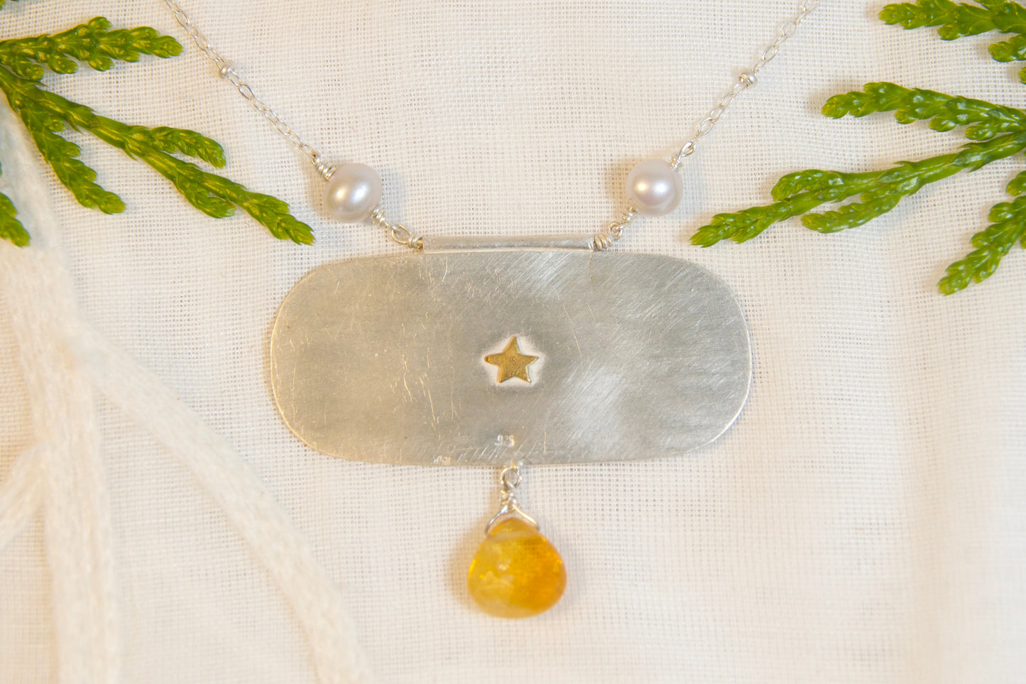 Necklace with a star pendant and citrine bead on a textured fabric background