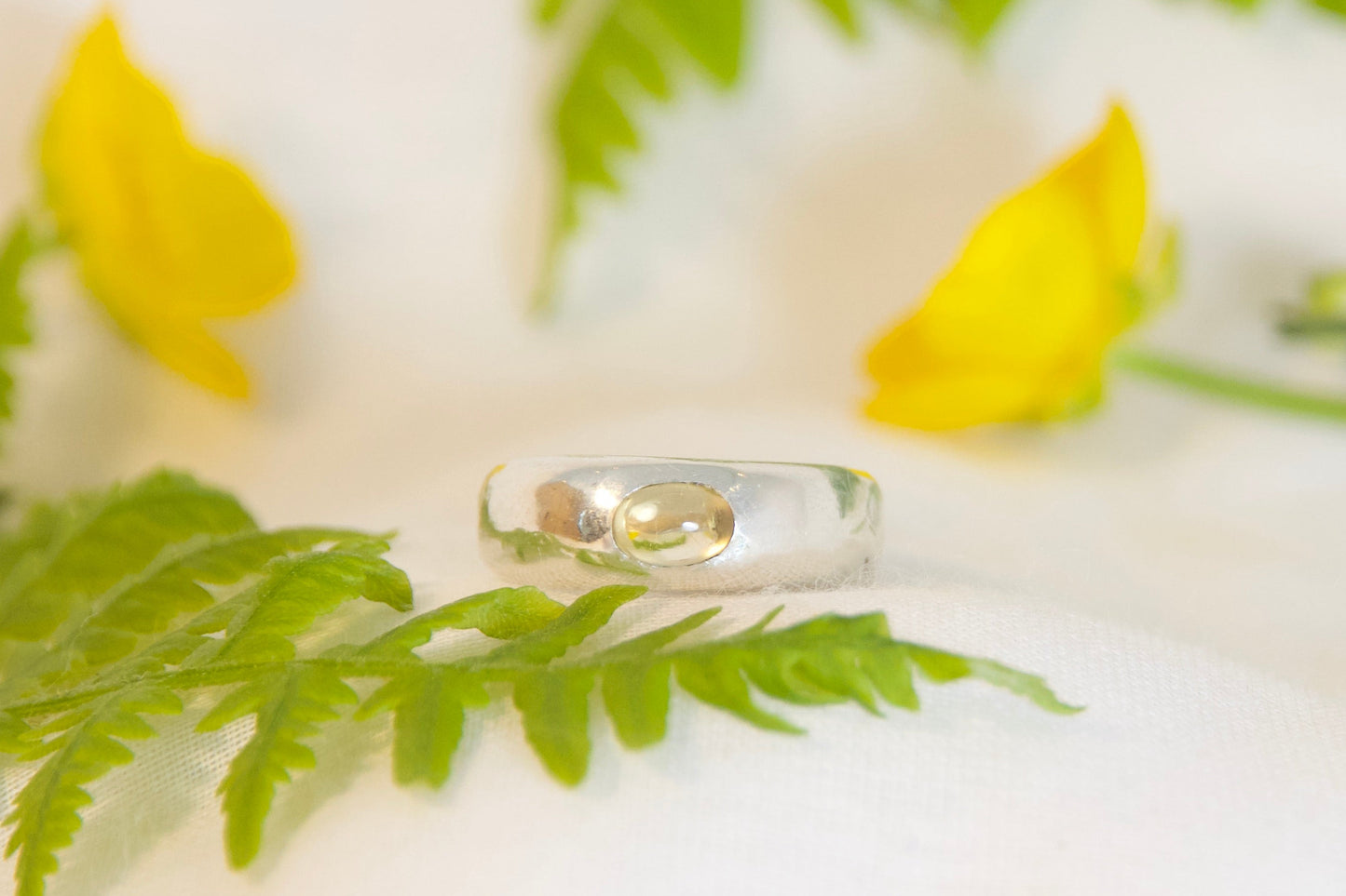 Silver ring on a white surface with green leaves and yellow flowers