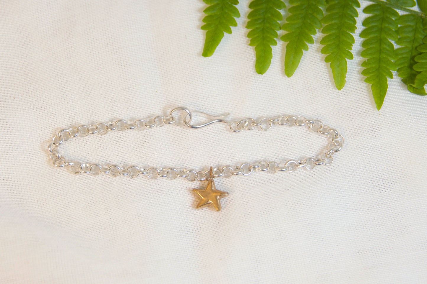 Silver bracelet with a star charm on a white fabric background with green leaves.