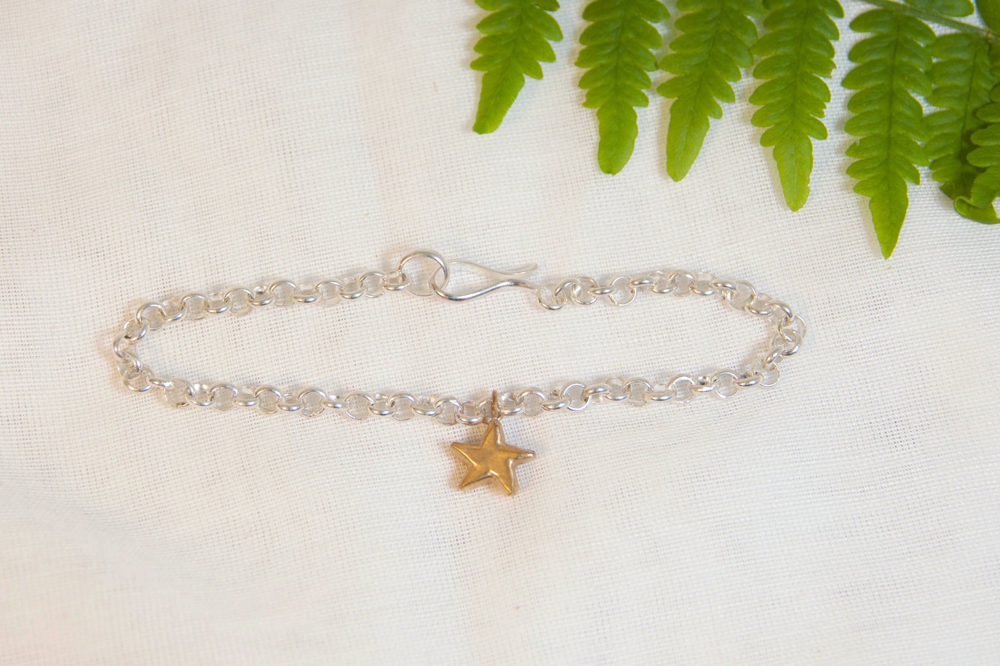 Silver bracelet with a star charm on a white fabric background with green leaves.