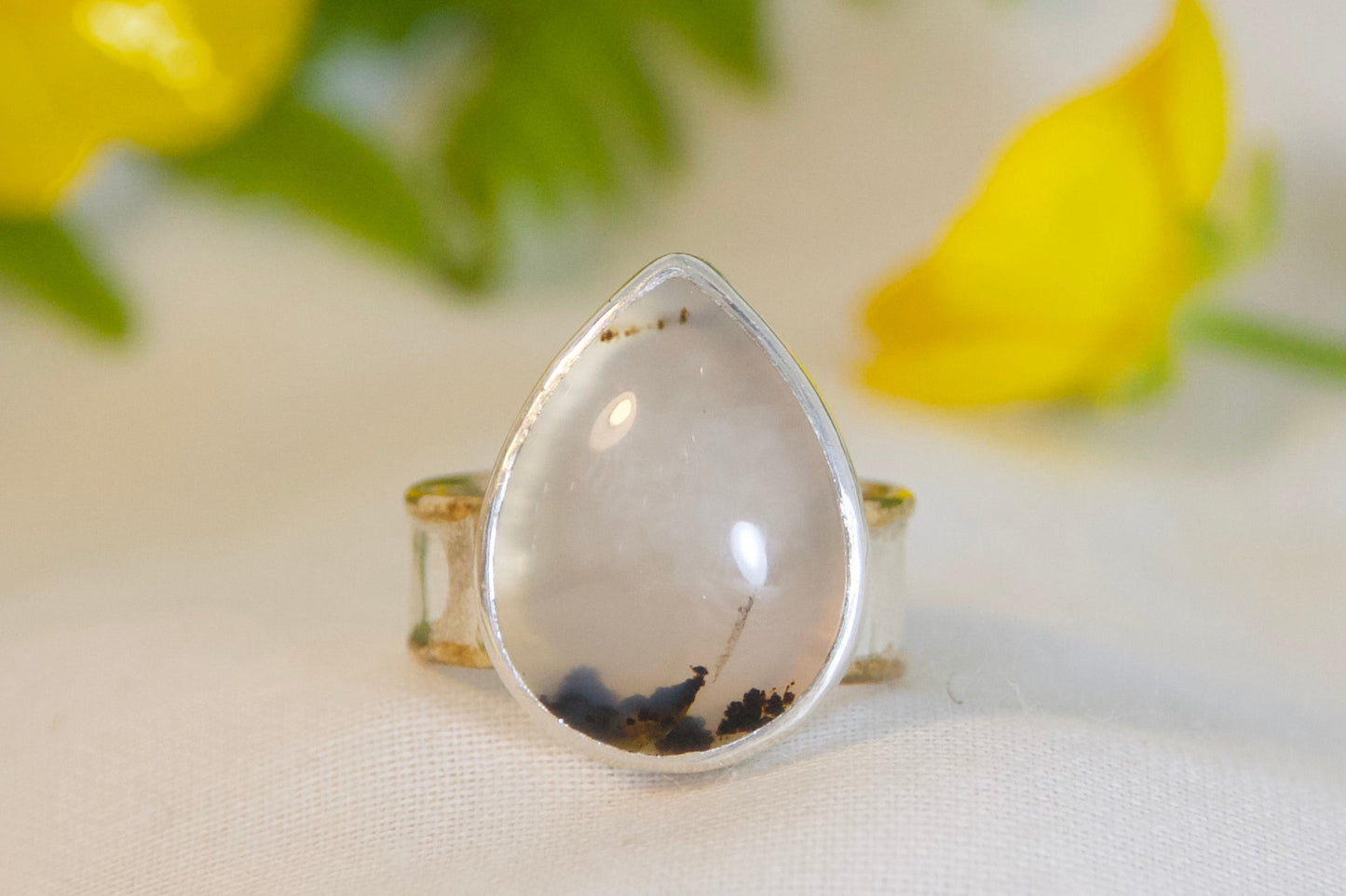 Teardrop-shaped ring with gold band on a white surface with green leaves and yellow flowers.