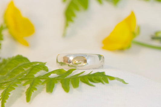 Silver ring on a white surface with yellow flowers and green leaves
