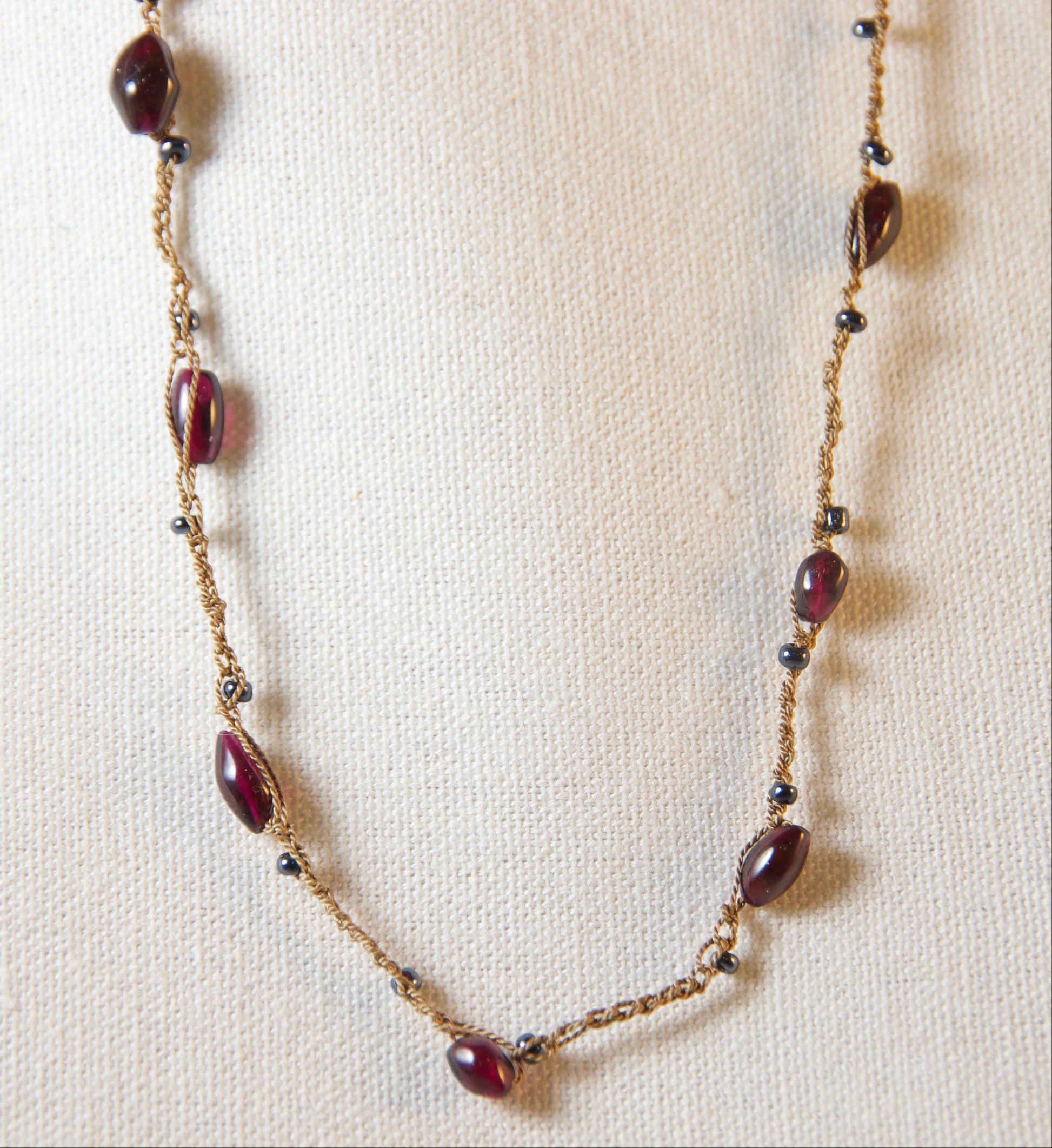 Beaded necklace with maroon beads on a beige fabric background
