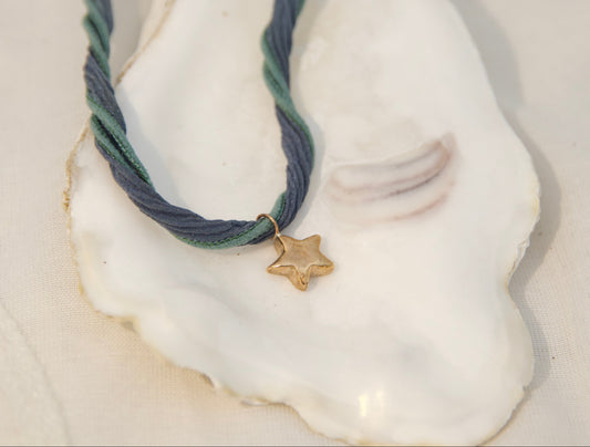 Hand made bronze star pendant on silk cord sitting on an oyster shell