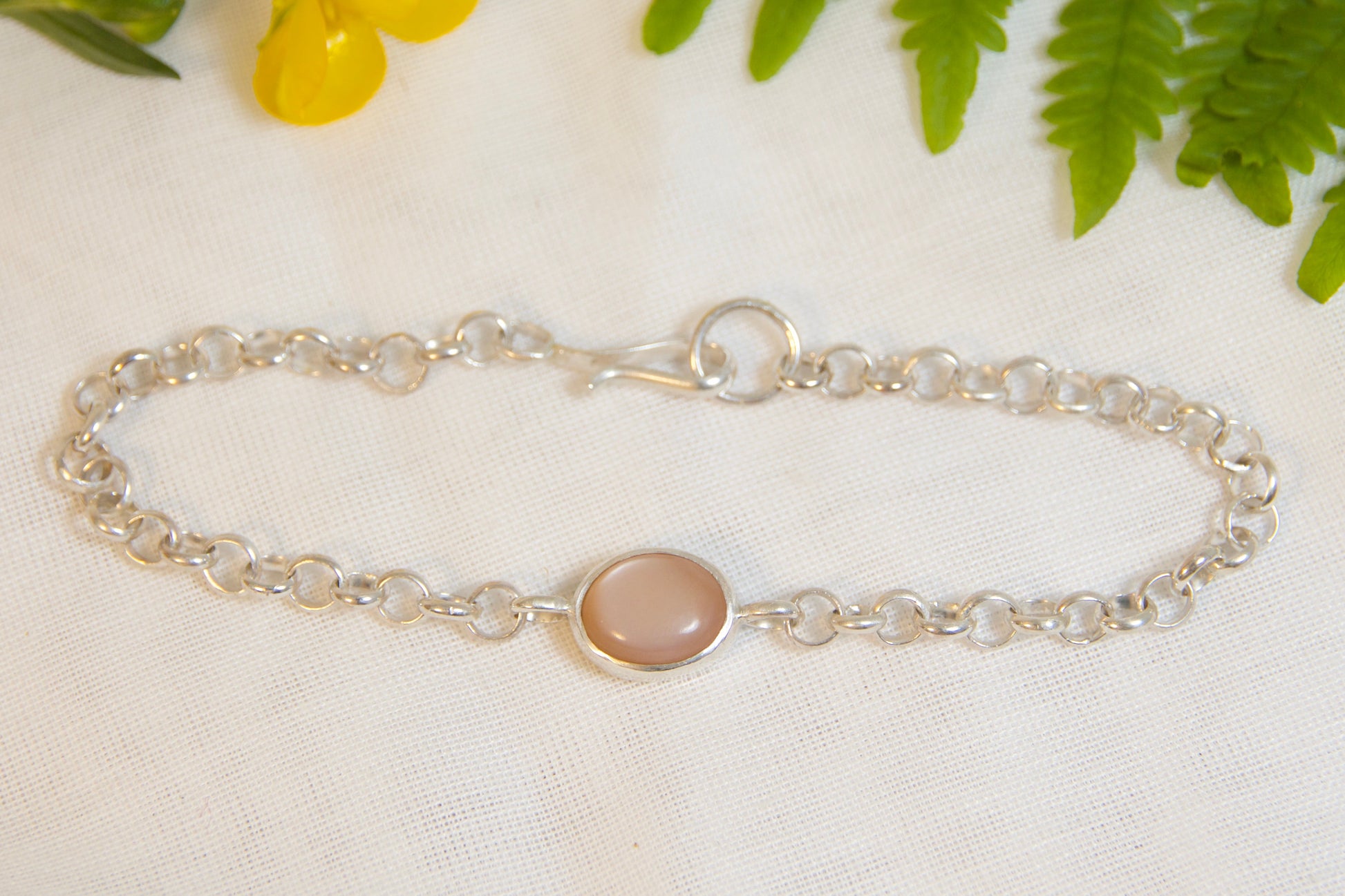 Silver bracelet with a pink gemstone on a white background with yellow flower and green leaves.