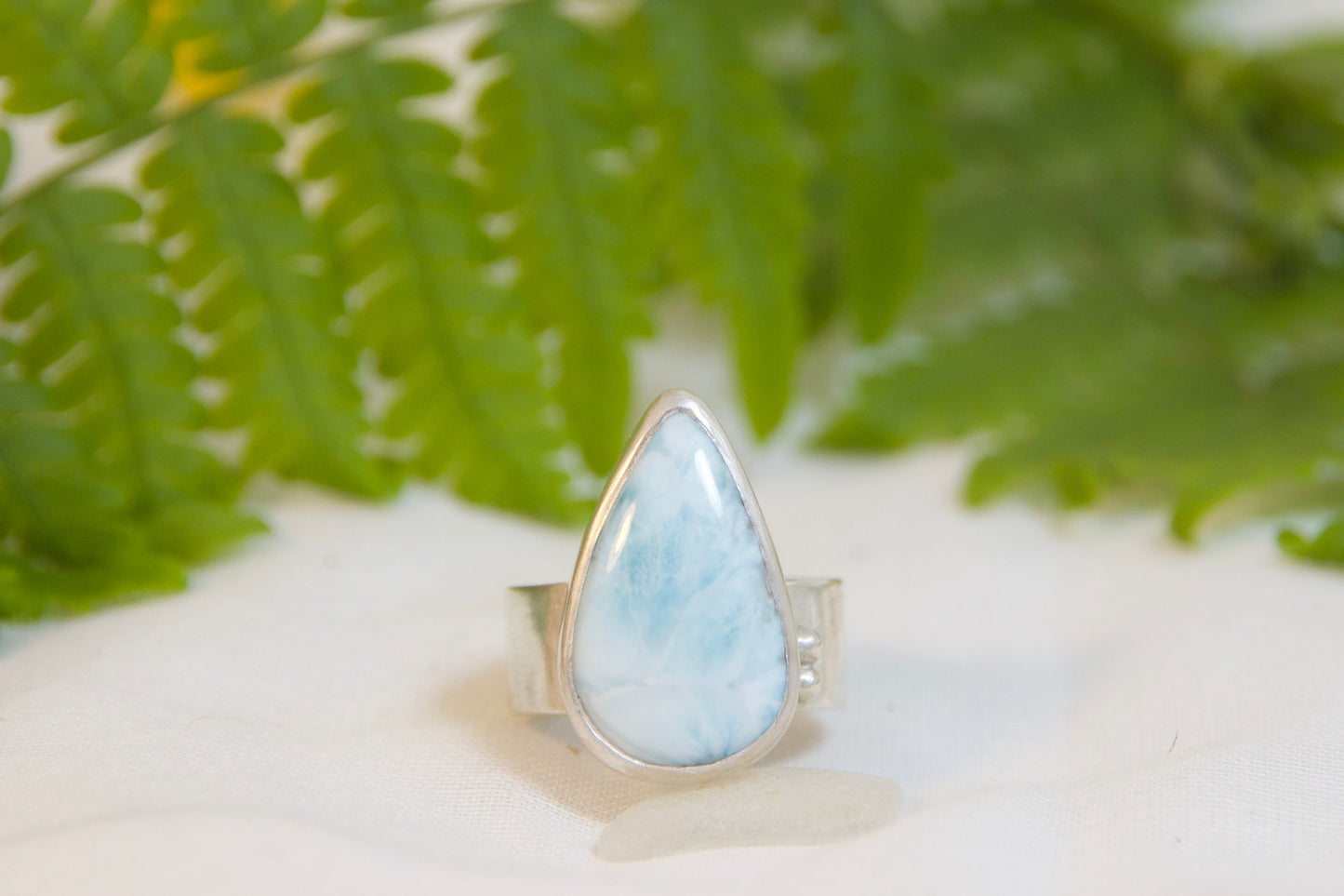 Ring with a larimar stone on a white surface with green leaves and yellow flowers in the background