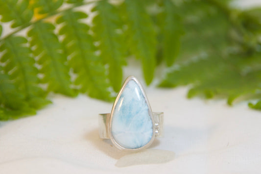 Ring with a larimar stone on a white surface with green leaves and yellow flowers in the background