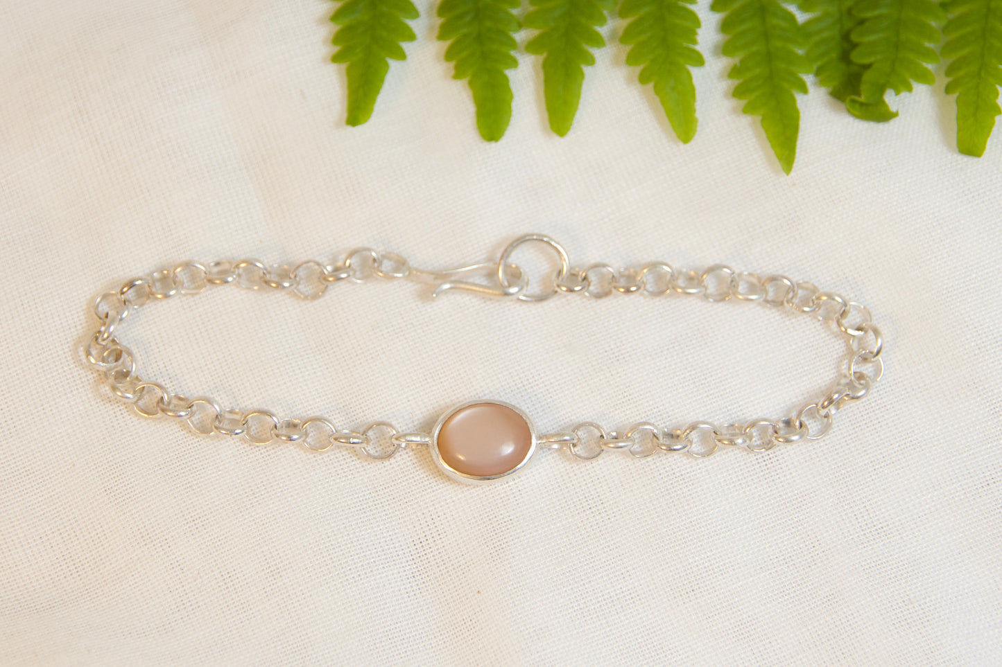 Silver bracelet with a round gemstone on a light surface with green leaves in the background