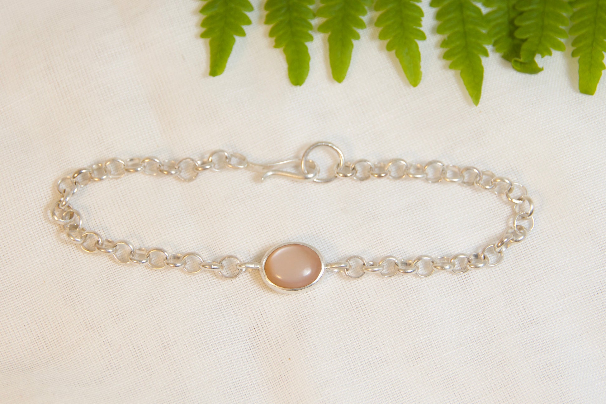 Silver bracelet with a round gemstone on a light surface with green leaves in the background