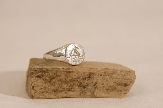Silver ring with a design on a wooden block against a beige background