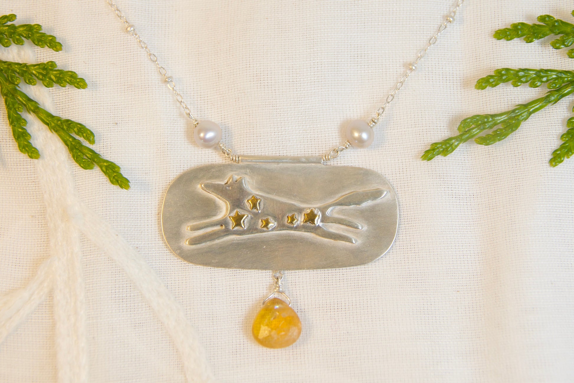 Necklace with a pendant on a textured fabric background with green leaves