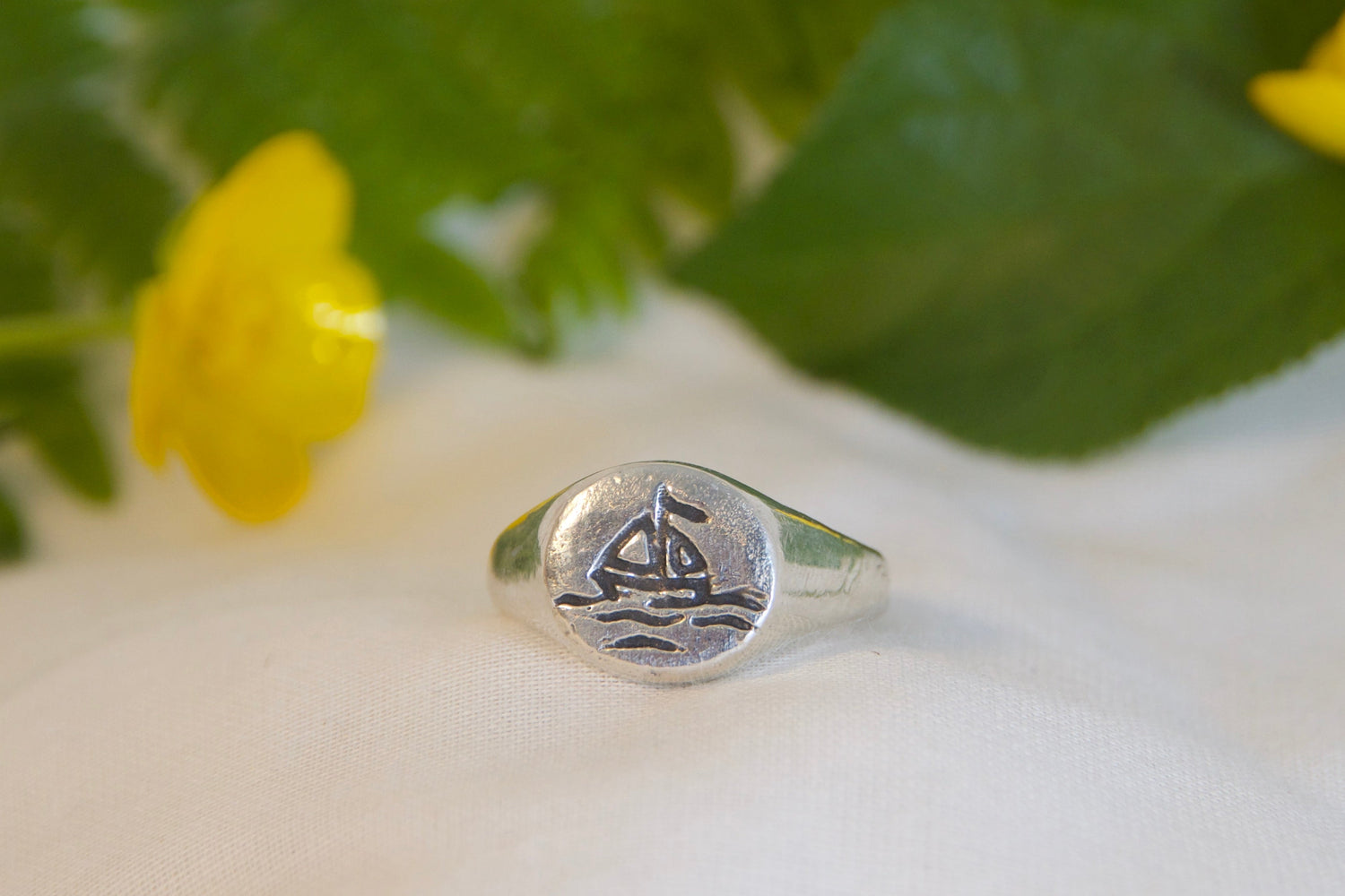 Silver ring with a floral design on a white surface with fern leaves and yellow flowers.
