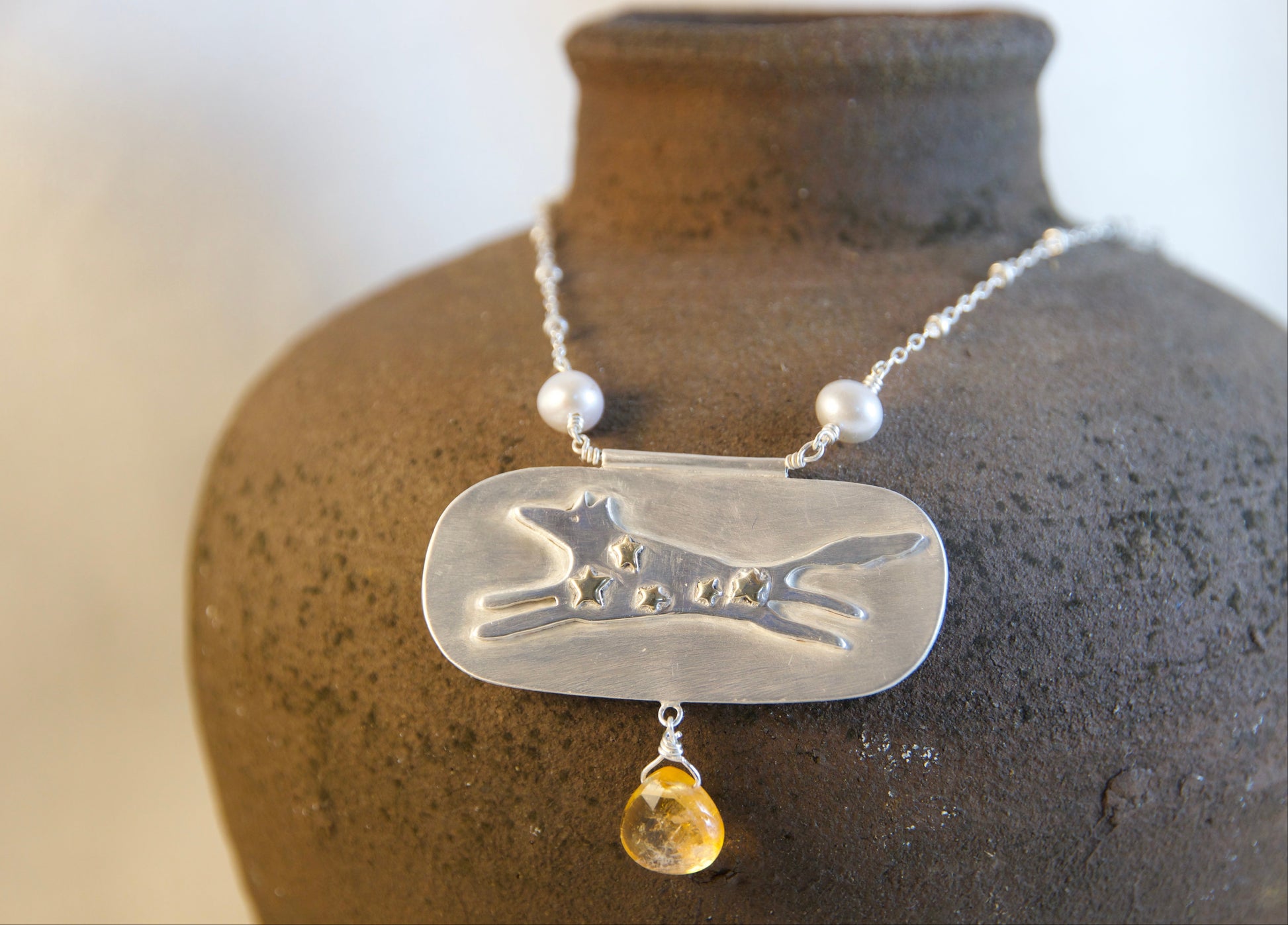 Necklace with a pendant featuring a dog design and a yellow gemstone on a textured vase.