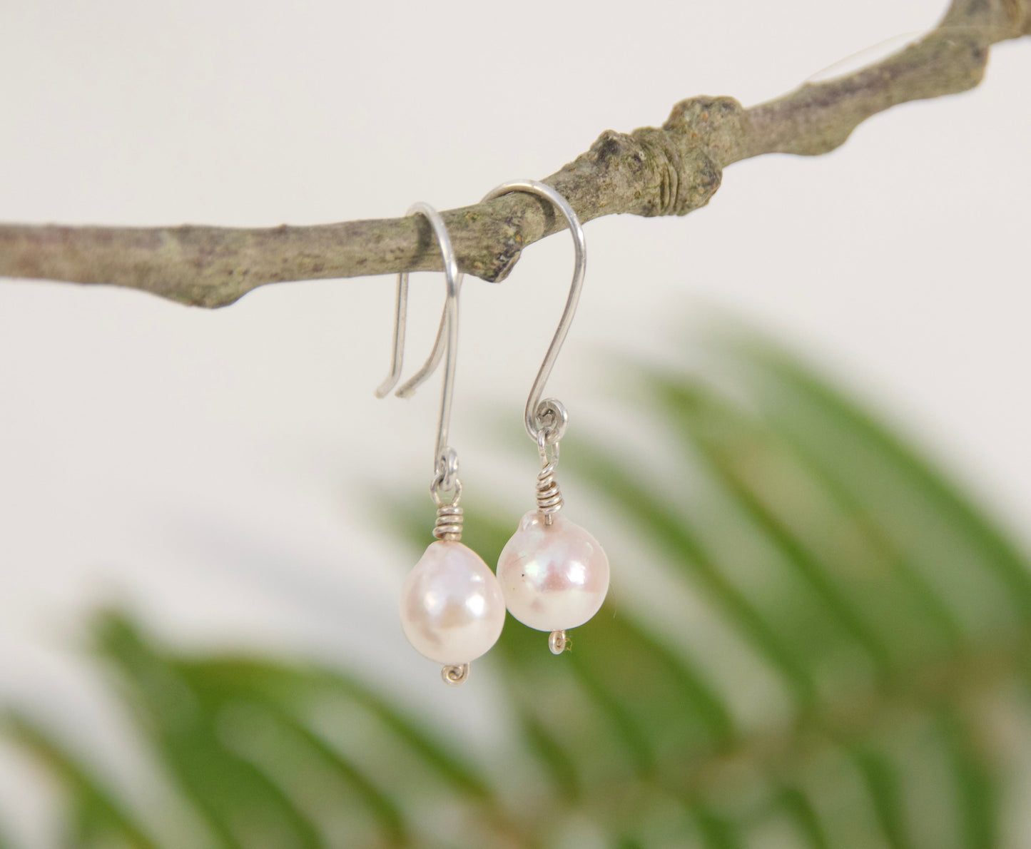 Pearl earrings hanging from a branch with a natural background