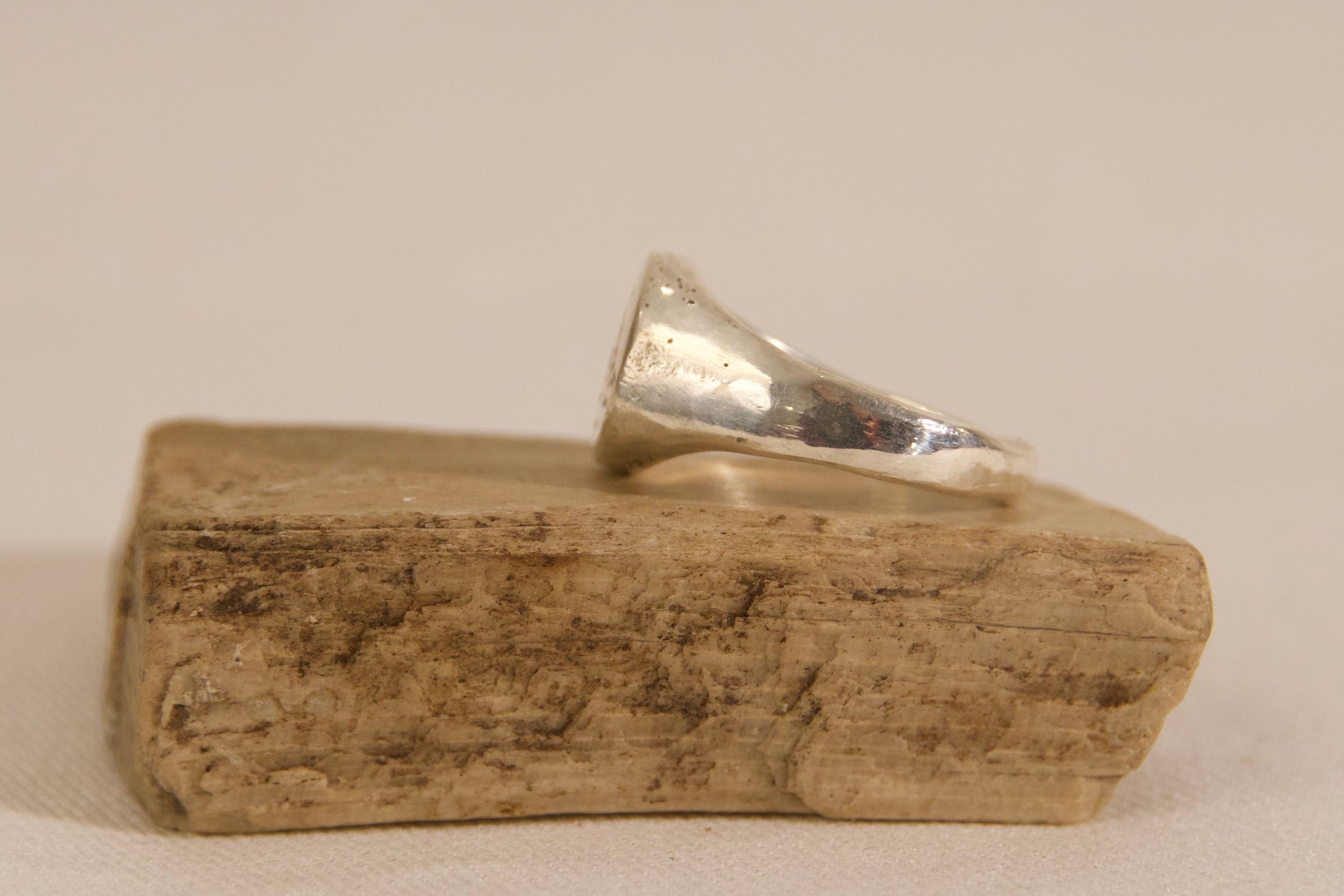 Silver ring on a wooden block against a beige background