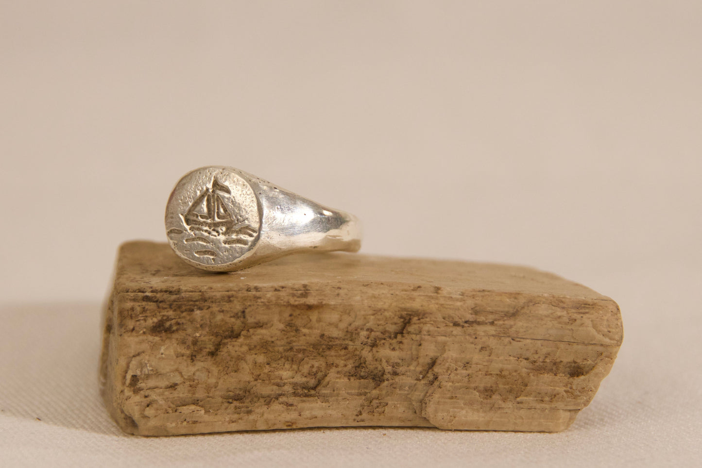 Silver ring with a sailboat design on a wooden block against a beige background