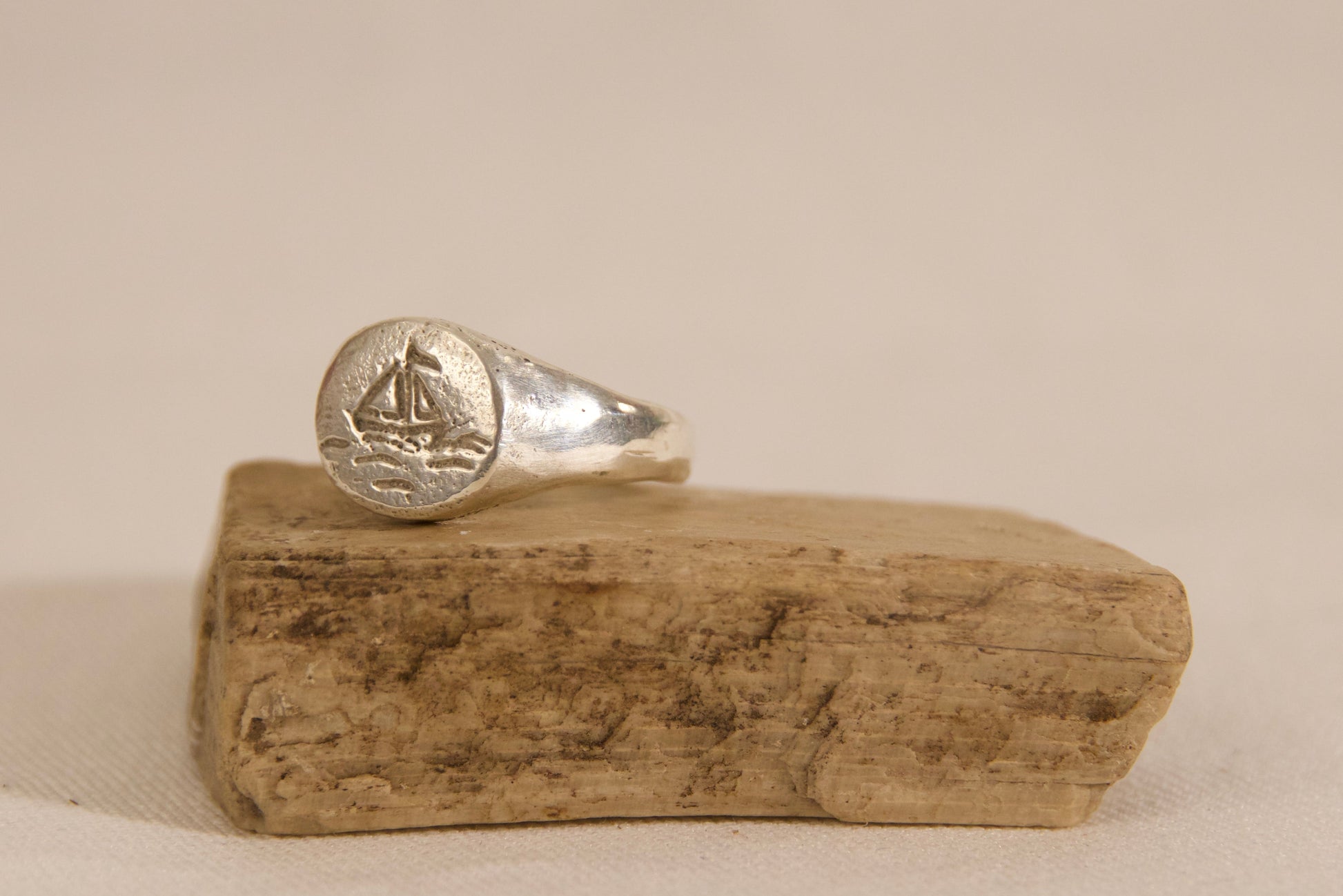 Silver ring with a sailboat design on a wooden block against a beige background