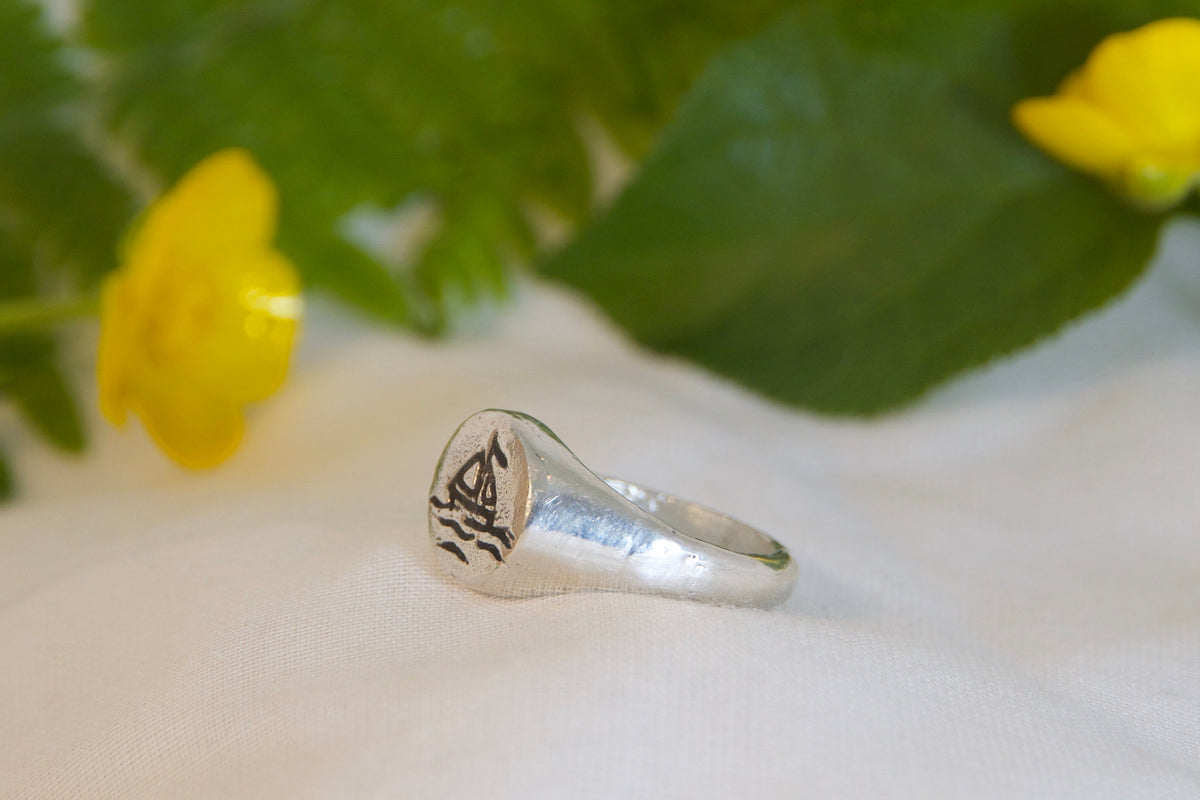 Silver ring with engraved design on a white surface with yellow flowers and green leaves.