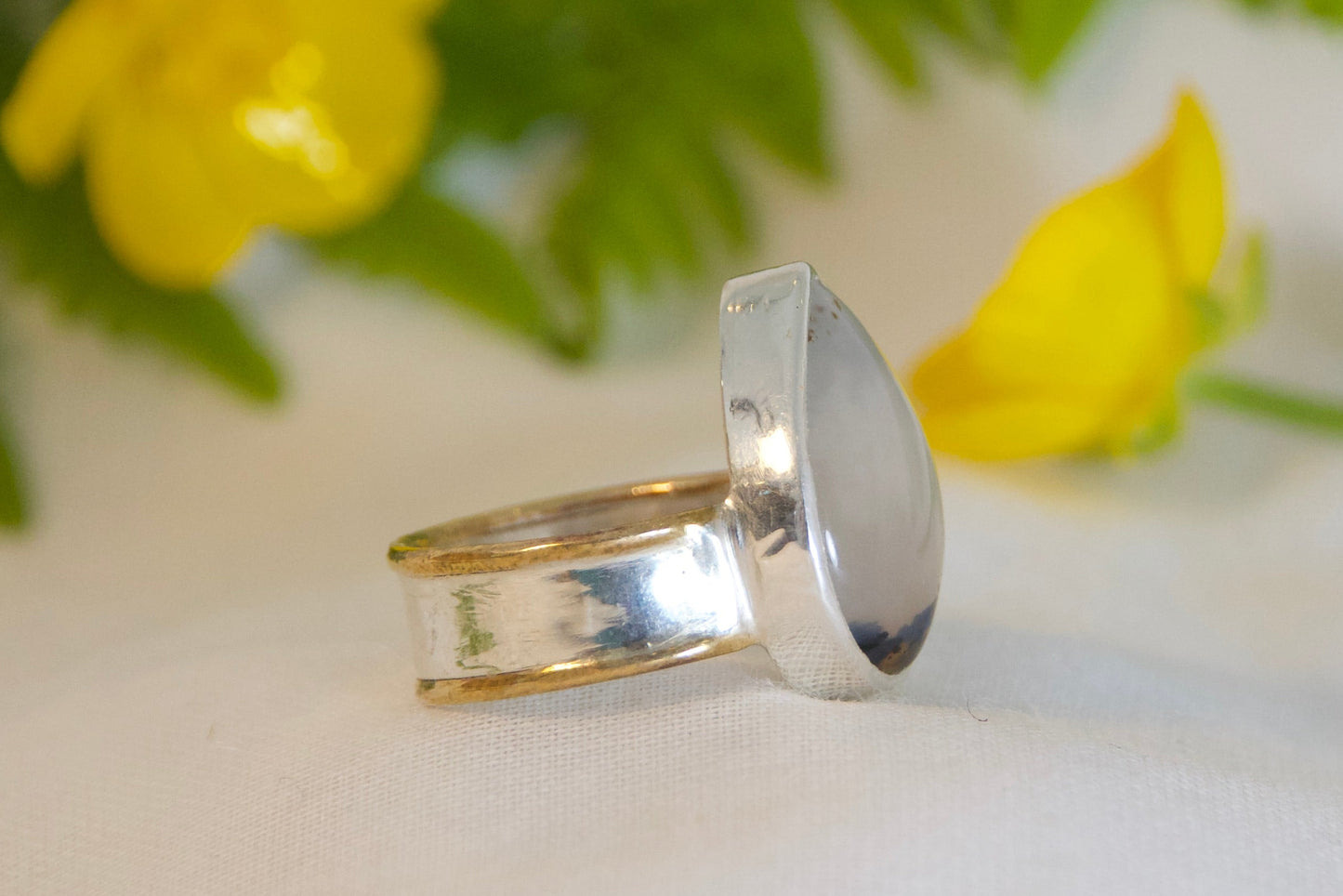 Silver ring on a white surface with green fern leaves and yellow flowers