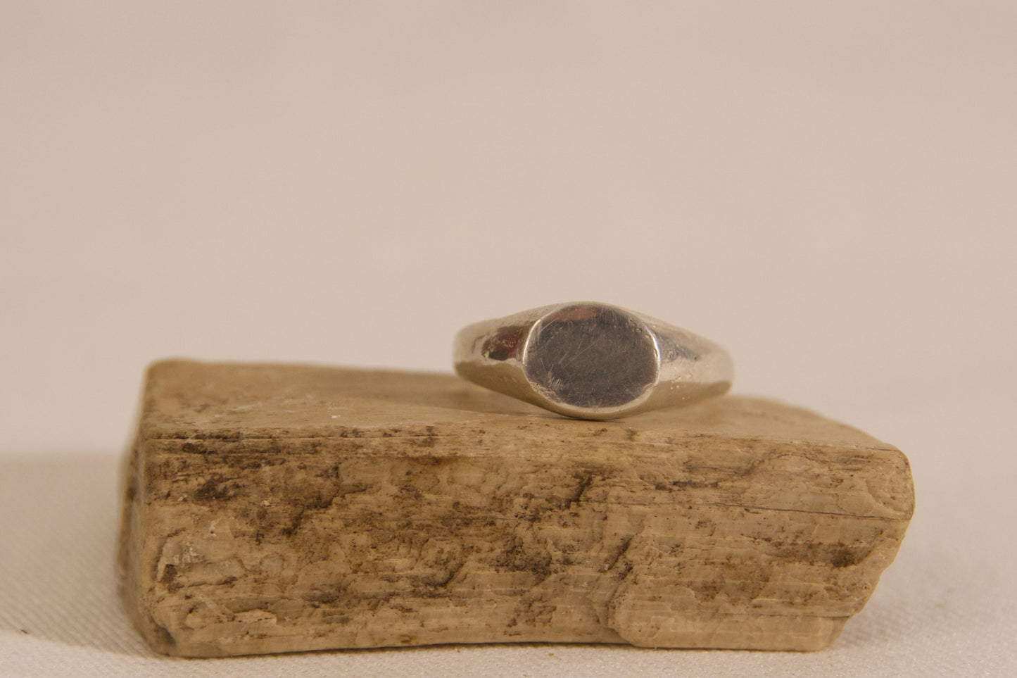 Silver ring on a piece of driftwood against a beige background