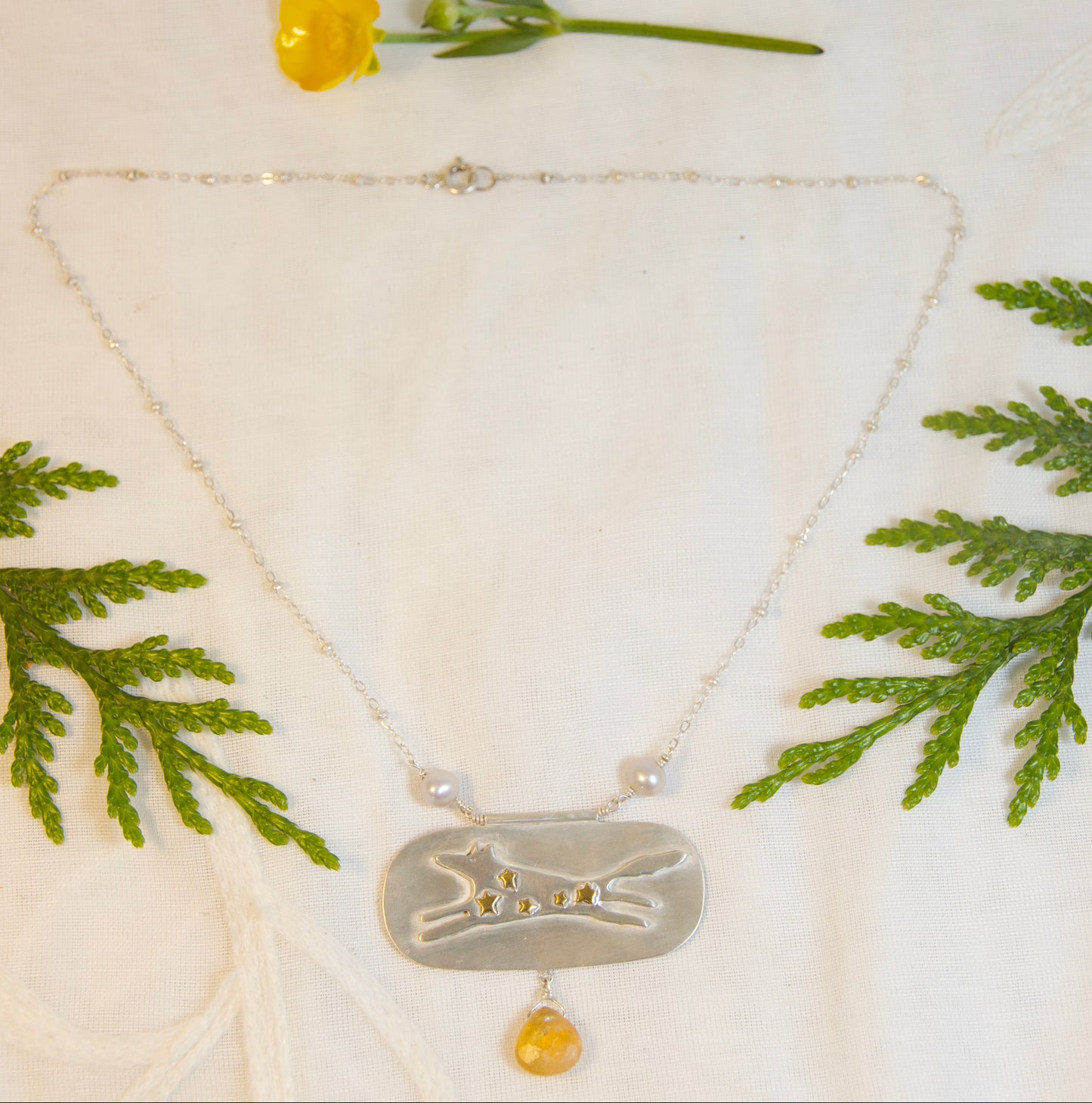 Necklace with a pendant on a white fabric background with green leaves and a yellow flower.
