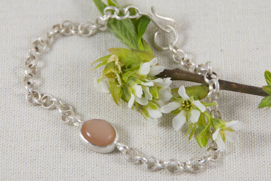 Silver bracelet with a pink stone on a branch with white flowers against a light gray background