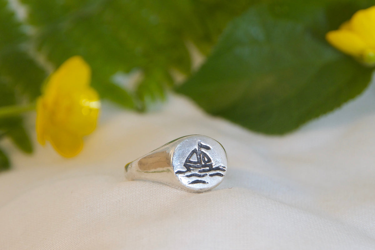 Silver ring with a design on a white surface with green leaves and yellow flowers.
