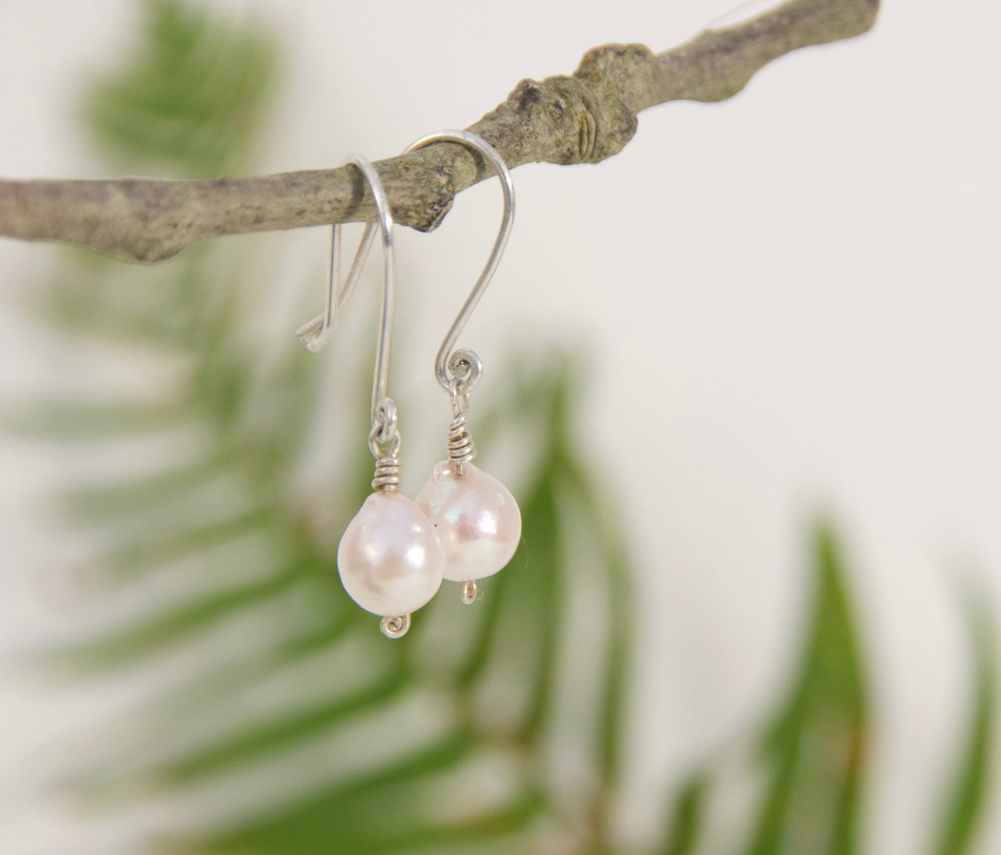 Pearl earrings hanging from a branch with a blurred natural background
