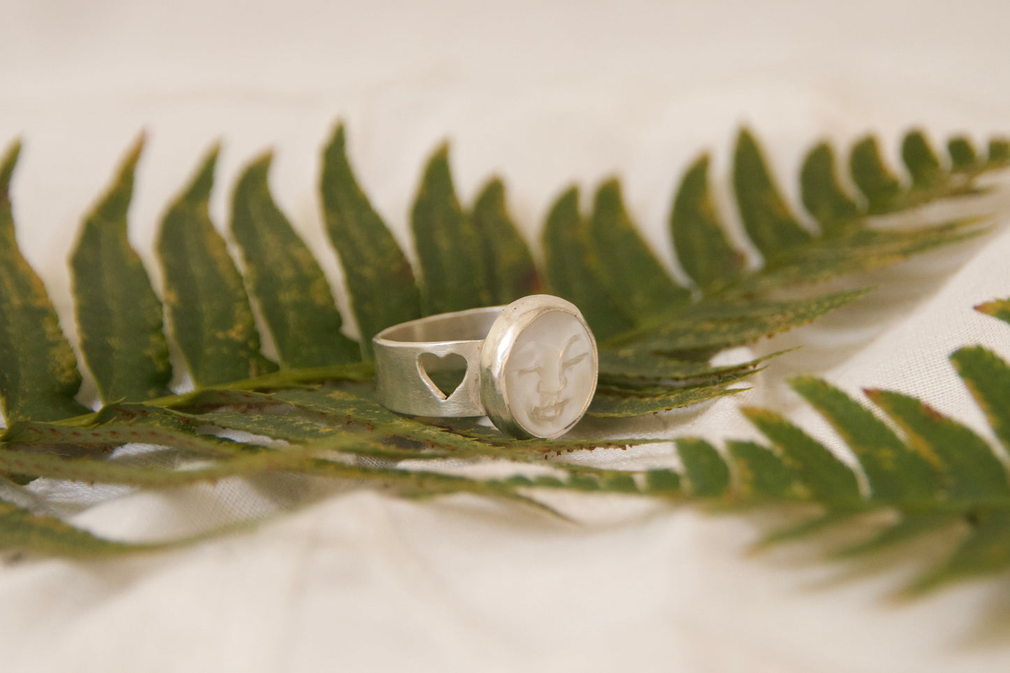 Hand carved face in Mother of pearl stone artfully set in sterling silver. Two skillfully cutout hearts symbolizing friendship and love 