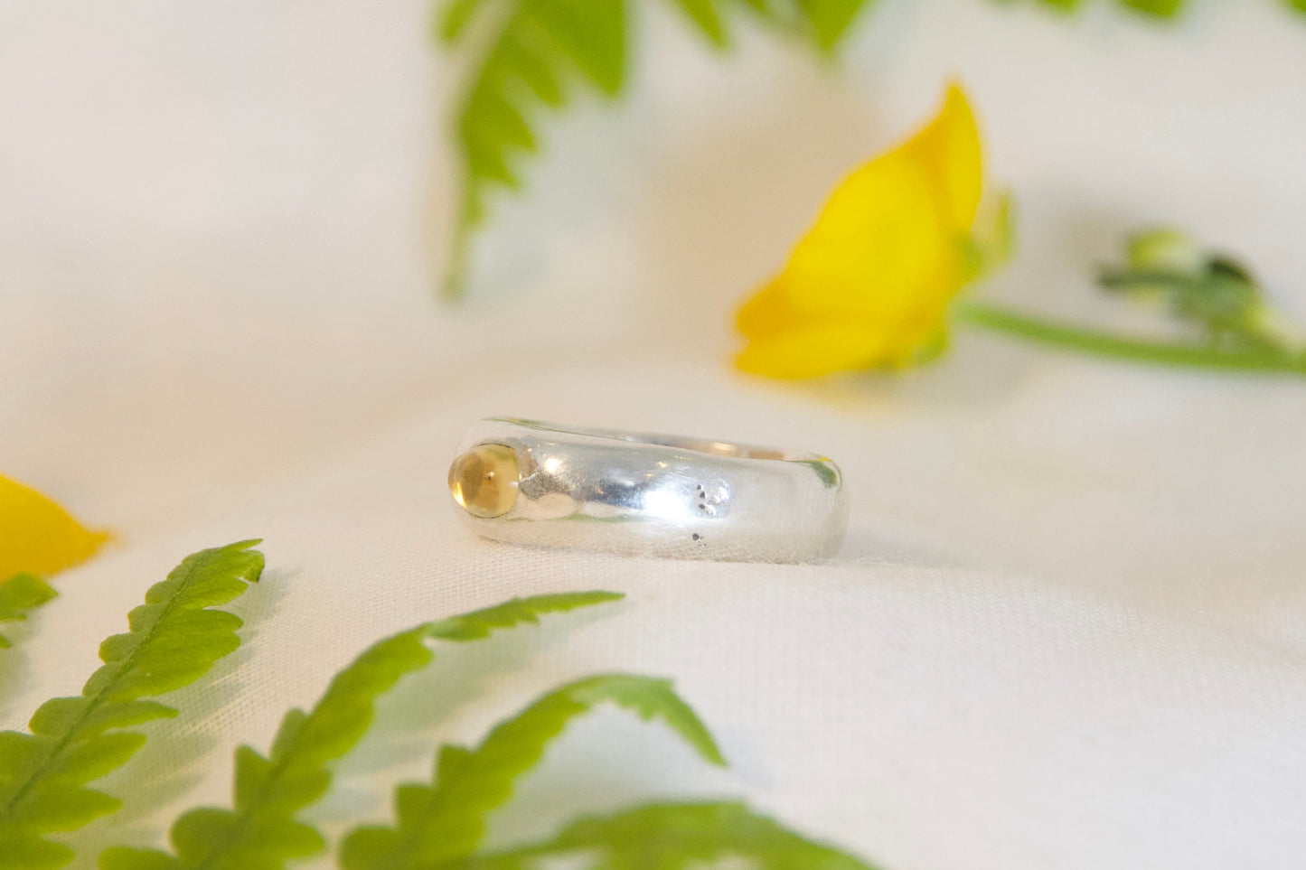 Silver ring on a white surface with green leaves and yellow flowers