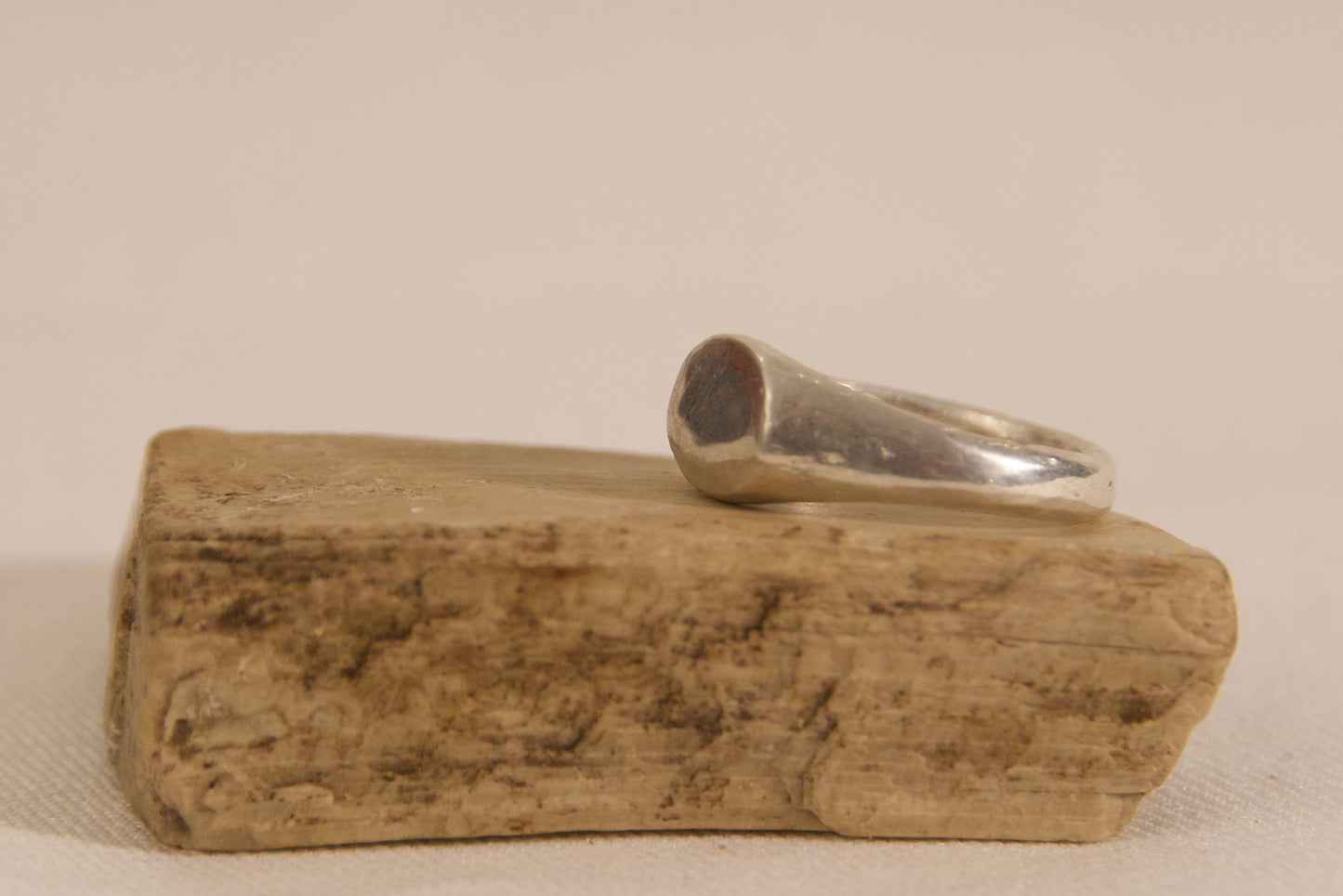 Silver ring on a wooden block against a beige background