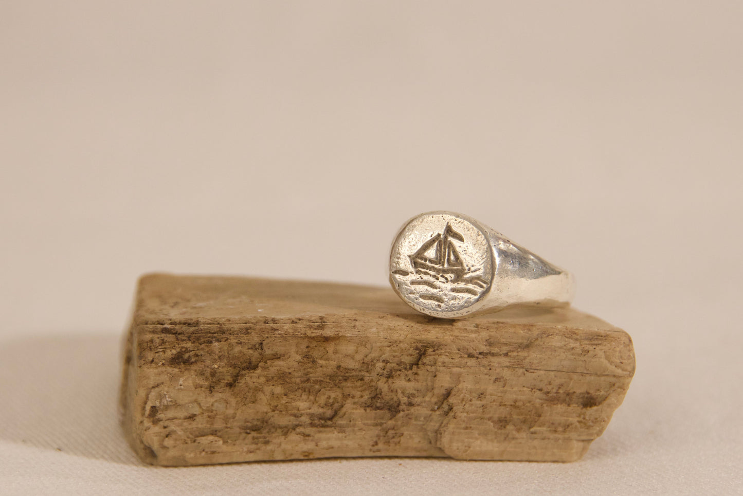 Silver ring with a design on a piece of driftwood against a beige background