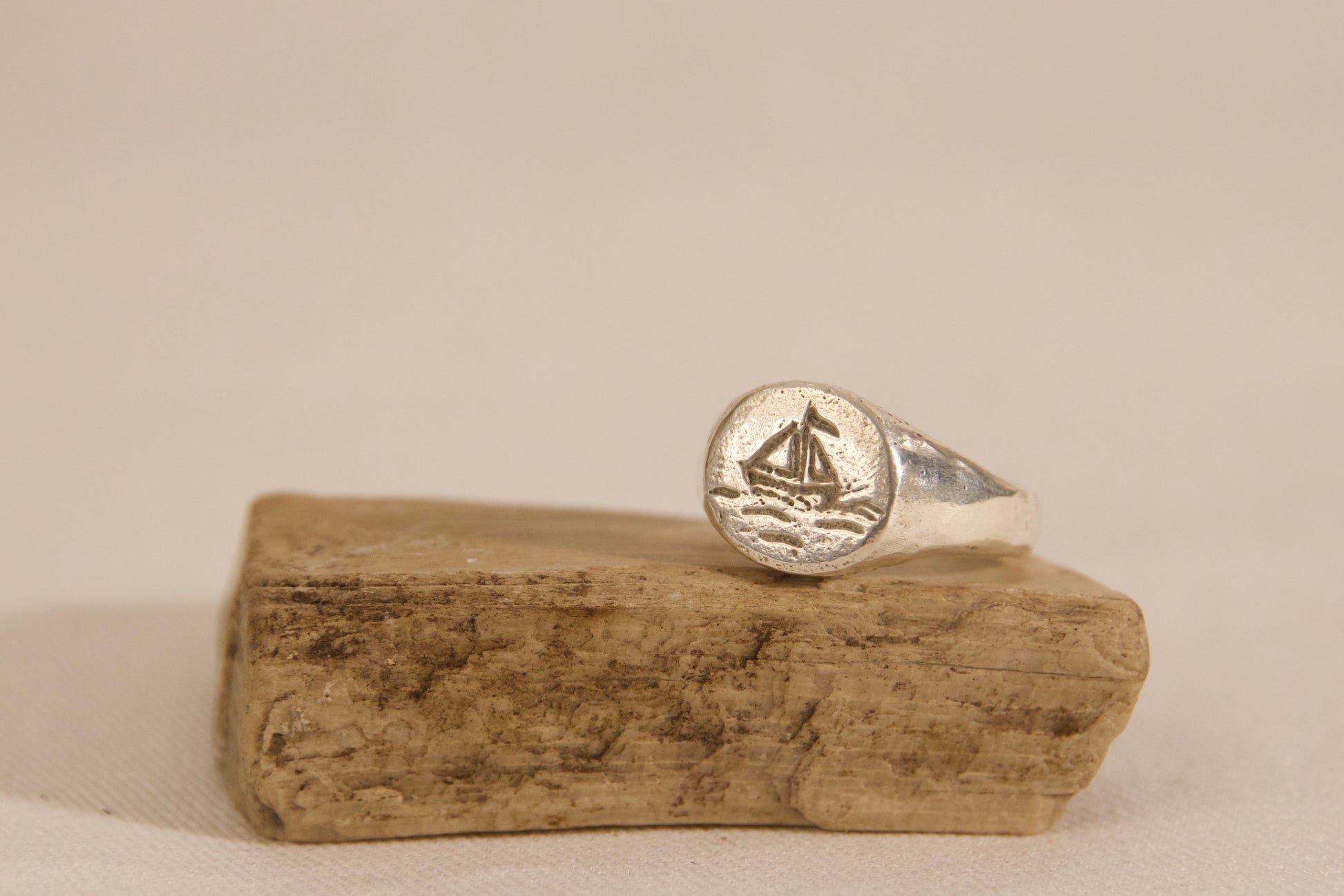 Silver ring with a design on a piece of driftwood against a beige background