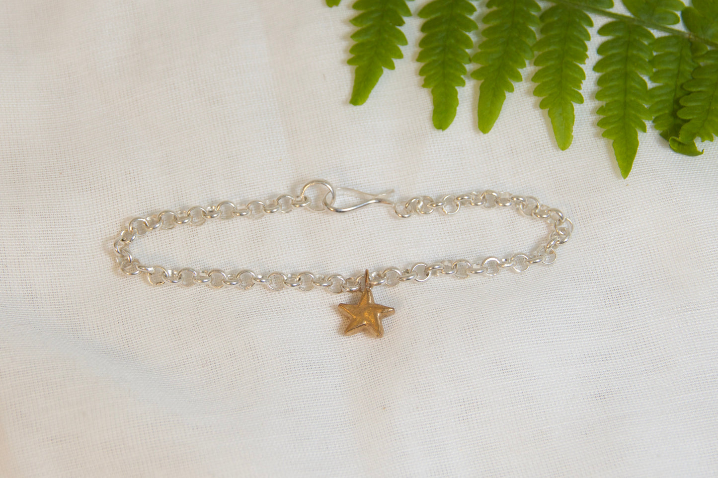 Silver bracelet with a star charm on a white fabric background with green leaves.