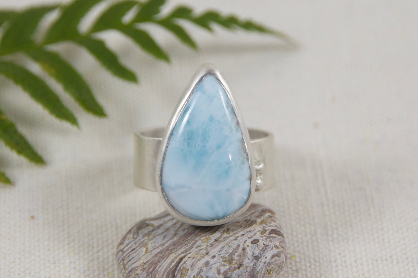 Ring with a teardrop-shaped light blue stone on a white background with a fern leaf.